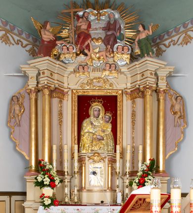 Zdjęcie nr 1: Ołtarz prostopadłościenny, murowany, ustawiony na jednym stopniu. Mensa drewniana, z marmurowym portatylem. W polu antependium rocaille’owy kartusz ujęty parą gałązek palmowych. 

Tabernakulum w formie drewnianej, prostopadłościennej skrzynki na wysokim cokole, o wklęsło-wypukłym rzucie; flankowane parą ustawionych ukośnie kolumienek o kompozytowych kapitelach, dźwigających wyłamane belkowanie. Drzwiczki w formie stojącego prostokąta, obite blachą miedzianą z aplikowanym kielichem z hostią oraz krzyżem na tle promienistej glorii. Nad nimi płaskorzeźbiony, stylizowany ornament rocaille’owy z muszlą palmetową pośrodku. Ścianki boczne dekorowane prostokątnymi płycinami zamkniętymi rocaille’ami z kwiatowymi zwisami. 

Nastawa ołtarzowa architektoniczna, jednokondygnacyjna ze zwieńczeniem, ustawiona na dwustrefowym cokole. Kondygnacja ujęta ustawionymi ukośnie: parą lizen, filarów i dwiema parami kolumn. Podpory dźwigają pełne belkowanie, wyłamane nad osią główną i osiami bocznymi. Podpory ustawione na bazach, o kapitelach kompozytowych; trzony kolumn gładkie, złocone. Na belkowaniu, na wewnętrznej parze podpór siedzące na obłokach figury aniołów. W polu środkowym nisza w formie stojącego prostokąta z obrazem Matki Boskiej Bieńkowskiej, ujęta profilowaną ramą. Nad polem środkowym łuk segmentowy, nadwieszony, zdobiony w polu stylizowanym ornamentem rocaille’owym. Nad łukiem i w zwieńczeniu cztery pary uskrzydlonych główek anielskich na obłokach. Zwieńczenie tworzy grupa rzeźbiarska z przedstawieniem Trójcy Świętej na tle obłoków i promienistej glorii. Filary od wewnątrz dekorowane zwisami utworzonymi z ornamentu rocaille’owego, różanych gałązek, słoneczników, drobnych kwiatów i owoców. Fryz zdobiony pojedynczymi, pięciopłatkowymi kwiatkami. Kondygnacja ujęta uszami w kształcie drapowanej kotary, obwiedzionej złotą lamówką, podtrzymywanej przez parę puttów. Putta ustawione frontalnie, ze skrzyżowanymi nogami, z jedną ręką uniesioną do góry, drugą spuszczoną w dół, z jednym skrzydłem od strony wewnętrznej, z pasem tkaniny spływającym z ramienia na biodra. Putta rzeźbione miękko; twarze owalne, pucułowate, z małymi oczami i ustami; włosy jasne, kędzierzawe. 

Struktura polichromowana w kolorze beżowym z różowymi detalami; kolumny, profile i ornamentyka złocone i srebrzone.
