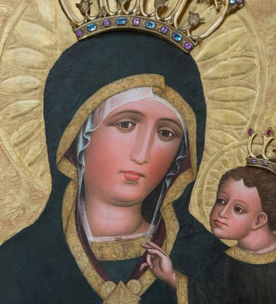Zdjęcie nr 5: Obraz w kształcie stojącego prostokąta z półpostaciowym przedstawieniem Madonny podtrzymującej lewą ręką Dzieciątko Jezus. Maria ukazana jest na wprost, lekko przechyloną w lewo głowę charakteryzuje owalna, pociągła twarz o wyrazistych oczach z nieznacznie przymkniętymi powiekami, długim, prostym nosie, niewielkich ustach o opadających kącikach, wyraźnie zaróżowionych policzkach oraz subtelnie zaznaczonym podbródku. Maria ubrana jest w ciemnogranatową suknię z szerokimi, dekoracyjnymi, złoconymi obszyciami dekoltu i wąskich mankietów. Na jej głowie jest biała, półprzejrzysta chusta widoczna spod osłaniającego całą sylwetkę ciemnogranatowego płaszcza o bordowej podszewce i szerokiej, złoconej, dekoracyjnej lamówce, spiętego na piersiach dużą, złoconą broszą w kształcie rombu z czterema kółkami przylegającymi do jego lekko wklęsłych boków. Prawą ręką o smukłej, wyprostowanej dłoni Maria wskazuje na trzymane na lewej ręce siedzące Dzieciątko. Zwrócony w trzech czwartych w prawo Jezus lekko pochyla się do przodu. Pociągłą, o trójkątnym obrysie szczęki twarz charakteryzują duże, wyraziste oczy o nieznacznie przymkniętych powiekach, długi, prosty nos oraz niewielkie usta. Krótkie, brązowe, skręcone włosy opadają parą pukli na czoło Dzieciątka. Ubrane jest ono w długą, ciemnogranatową suknię z szerokimi, dekoracyjnymi, złoconymi lamówkami, spod której widoczne są bose stopy. Jezus prawą dłoń unosi w geście błogosławieństwa, lewą trzyma wspartą na kolanach zamkniętą księgę w zielonej oprawie. Głowy postaci okalają ryte w gruncie podobrazia nimby z motywami eliptycznych promieni ujętych wąskim okręgiem, dodatkowo wieńczą je złocone, kameryzowane korony otwarte. Złocone tło przedstawienia zdobi grawerowana wić roślinna. Obraz ujęty jest złoconą ramą w formie ażurowego układu liści akantu.      