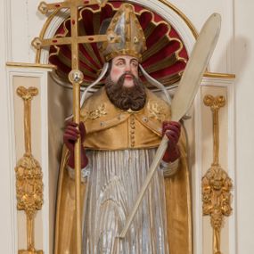 Zdjęcie nr 1: Całopostaciowa, drążona z tyłu figura św. Wojciecha stojącego w układzie frontalnym, w nieznacznym kontrapoście, na niewielkim, prostopadłościennym postumencie. Pociągłą twarz świętego charakteryzują sumarycznie opracowane rysy z szeroko rozstawionymi, lekko przymkniętymi oczami, zarumienione policzki i czubek nosa oraz długi, brązowy, skręcony zarost. Święty ubrany jest w strój pontyfikalny składający się ze złoconej alby, srebrzonej komży, złoconego mucetu oraz złoconej kapy zdobionej motywami roślinnymi z obszyciem z kaboszonami. Na głowie ma złocono-srebrzoną infułę z dekoracją z kaboszonów i opadającymi na ramiona srebrzonymi taśmami. Dłonie biskupa osłaniają czerwone rękawiczki, a stopy czerwone buty. W prawej ręce trzyma krzyż pastoralny, a lewej wiosło.