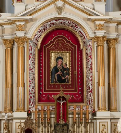 Zdjęcie nr 2: Ołtarz architektoniczny, dwukondygnacyjny, trójosiowy, ze zwieńczeniem. Ołtarz murowany, prostopadłościenny z marmurowym antepedium. Tabernakulum w formie prostopadłościennej, metalowej szafki ujętej parą ażurowych spływów wolutowych w formie stylizowanych wici akantowych. Drzwiczki, w kształcie zbliżonym do kwadratu, zdobione motywem krzyża i banderoli z napisem „IHS” ujętych kłosami zboża i kiściami winnej latorośli. Tron wystawienia w formie baldachimu wspartego na 4 kolumienkach. Krawędź zwieńczenia ujęta jest ornamentyką roślinną, w motywem kartusza z krzyżem po środku. Oś środkowa retabulum osadzona na wysokim, zdwojonym cokole o zryzalitowanych bokach. Pierwszą kondygnację ujmują dwie pary kolumn o kanelowanych trzonach i korynckich kapitelach, z czego wewnętrzne wysunięte względem lica nastawy, wspierających wyłamujące się ponad nimi belkowanie, w partii architrawu przybierające kształt  półkolistego łuku nadwieszonego; całość wieńczy forma trójkątnego przyczółka. Druga kondygnacja ujęta parą osadzonych na cokołach kolumn o trzonach zdobionych wicią winnej latorośli, wspierających delikatnie wyłamujące się ponad nimi belkowanie przerwane w partii fryzu u gzymsu. Zwieńczenie w formie trójkątnego, przerwanego przyczółka. W strefie zryzalitowanych po bokach cokołów osi bocznych para półkoliście zamkniętych bramek. Krawędzie zewnętrzne kondygnacji osi bocznych ujęte pojedynczymi kolumnami dźwigającymi wyłamujące się ponad nimi belkowanie wieńczące, będące przedłużeniem belkowania osi środkowej.  Pola cokołu retabulum wypełnione motywami ornamentyki roślinnej, w partii fryzu motywy małżowinowo-chrząstkowe. Druga kondygnacja osi środkowej ujęta parą ażurowych, małżowinowo-chrząstkowych uszaków, szczyt zwieńczenia w formie promienistej glorii z owalnym medalionem ujętym wieńcem obłoków, z monogramem imienia Jezus. Pola osi bocznych w dolnej partii zdobione motywami małżowinowo-chrząstkowego kartusza, w górnej owocowo-kwiatowymi festonami. Skrajne pola cokołu retabulum wypełnia para wizerunków – św. Pawła po prawej stronie i św. Piotra po lewej. Pole pierwszej kondygnacji osi środkowej ma formę płytkiej wnęki w kształcie stojącego prostokąta zamkniętego półkolistym łukiem nadwieszonym, ujętej bogato rzeźbioną ramą z motywem ornamentu małżowinowo-chrząstkowego, w środku obraz Matki Boskiej z Dzieciątkiem. Pole drugiej kondygnacji wypełnia obraz w kształcie leżącego prostokąta, ujęty szeroką ramą z uszakami w narożach, zdobioną ornamentem małżowinowo-chrząstkowym. Po bokach para półkoliście zamkniętych niszy z motywem konchy, wypełnionych parą figur – po prawej stronie św. Dominika, po lewej św. Antoni (?). Pola osi bocznych artykułuje para zamkniętych półkoliście niszy z motywami konchy, z parą rzeźb – św. Stanisława po prawej stronie i św. Wojciecha po lewej.  W szczycie osi bocznych pośrodku para rzeźb flankujących zwieńczenie ołtarza – po prawej stronie św. Wacława, po lewej św. Kazimierza, na końcach para figur aniołów. Struktura polichromowana w odcieniach koloru kremowego i beżowego, detal architektoniczny i ornamentyka złocone i srebrzone.