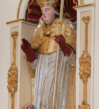 Zdjęcie nr 15: Ołtarz architektoniczny, dwukondygnacyjny, trójosiowy, ze zwieńczeniem. Ołtarz murowany, prostopadłościenny z marmurowym antepedium. Tabernakulum w formie prostopadłościennej, metalowej szafki ujętej parą ażurowych spływów wolutowych w formie stylizowanych wici akantowych. Drzwiczki, w kształcie zbliżonym do kwadratu, zdobione motywem krzyża i banderoli z napisem „IHS” ujętych kłosami zboża i kiściami winnej latorośli. Tron wystawienia w formie baldachimu wspartego na 4 kolumienkach. Krawędź zwieńczenia ujęta jest ornamentyką roślinną, w motywem kartusza z krzyżem po środku. Oś środkowa retabulum osadzona na wysokim, zdwojonym cokole o zryzalitowanych bokach. Pierwszą kondygnację ujmują dwie pary kolumn o kanelowanych trzonach i korynckich kapitelach, z czego wewnętrzne wysunięte względem lica nastawy, wspierających wyłamujące się ponad nimi belkowanie, w partii architrawu przybierające kształt  półkolistego łuku nadwieszonego; całość wieńczy forma trójkątnego przyczółka. Druga kondygnacja ujęta parą osadzonych na cokołach kolumn o trzonach zdobionych wicią winnej latorośli, wspierających delikatnie wyłamujące się ponad nimi belkowanie przerwane w partii fryzu u gzymsu. Zwieńczenie w formie trójkątnego, przerwanego przyczółka. W strefie zryzalitowanych po bokach cokołów osi bocznych para półkoliście zamkniętych bramek. Krawędzie zewnętrzne kondygnacji osi bocznych ujęte pojedynczymi kolumnami dźwigającymi wyłamujące się ponad nimi belkowanie wieńczące, będące przedłużeniem belkowania osi środkowej.  Pola cokołu retabulum wypełnione motywami ornamentyki roślinnej, w partii fryzu motywy małżowinowo-chrząstkowe. Druga kondygnacja osi środkowej ujęta parą ażurowych, małżowinowo-chrząstkowych uszaków, szczyt zwieńczenia w formie promienistej glorii z owalnym medalionem ujętym wieńcem obłoków, z monogramem imienia Jezus. Pola osi bocznych w dolnej partii zdobione motywami małżowinowo-chrząstkowego kartusza, w górnej owocowo-kwiatowymi festonami. Skrajne pola cokołu retabulum wypełnia para wizerunków – św. Pawła po prawej stronie i św. Piotra po lewej. Pole pierwszej kondygnacji osi środkowej ma formę płytkiej wnęki w kształcie stojącego prostokąta zamkniętego półkolistym łukiem nadwieszonym, ujętej bogato rzeźbioną ramą z motywem ornamentu małżowinowo-chrząstkowego, w środku obraz Matki Boskiej z Dzieciątkiem. Pole drugiej kondygnacji wypełnia obraz w kształcie leżącego prostokąta, ujęty szeroką ramą z uszakami w narożach, zdobioną ornamentem małżowinowo-chrząstkowym. Po bokach para półkoliście zamkniętych niszy z motywem konchy, wypełnionych parą figur – po prawej stronie św. Dominika, po lewej św. Antoni (?). Pola osi bocznych artykułuje para zamkniętych półkoliście niszy z motywami konchy, z parą rzeźb – św. Stanisława po prawej stronie i św. Wojciecha po lewej.  W szczycie osi bocznych pośrodku para rzeźb flankujących zwieńczenie ołtarza – po prawej stronie św. Wacława, po lewej św. Kazimierza, na końcach para figur aniołów. Struktura polichromowana w odcieniach koloru kremowego i beżowego, detal architektoniczny i ornamentyka złocone i srebrzone.