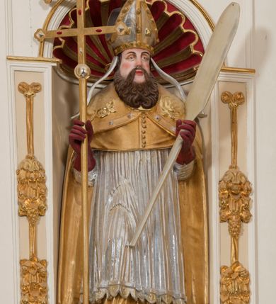 Zdjęcie nr 9: Ołtarz architektoniczny, dwukondygnacyjny, trójosiowy, ze zwieńczeniem. Ołtarz murowany, prostopadłościenny z marmurowym antepedium. Tabernakulum w formie prostopadłościennej, metalowej szafki ujętej parą ażurowych spływów wolutowych w formie stylizowanych wici akantowych. Drzwiczki, w kształcie zbliżonym do kwadratu, zdobione motywem krzyża i banderoli z napisem „IHS” ujętych kłosami zboża i kiściami winnej latorośli. Tron wystawienia w formie baldachimu wspartego na 4 kolumienkach. Krawędź zwieńczenia ujęta jest ornamentyką roślinną, w motywem kartusza z krzyżem po środku. Oś środkowa retabulum osadzona na wysokim, zdwojonym cokole o zryzalitowanych bokach. Pierwszą kondygnację ujmują dwie pary kolumn o kanelowanych trzonach i korynckich kapitelach, z czego wewnętrzne wysunięte względem lica nastawy, wspierających wyłamujące się ponad nimi belkowanie, w partii architrawu przybierające kształt  półkolistego łuku nadwieszonego; całość wieńczy forma trójkątnego przyczółka. Druga kondygnacja ujęta parą osadzonych na cokołach kolumn o trzonach zdobionych wicią winnej latorośli, wspierających delikatnie wyłamujące się ponad nimi belkowanie przerwane w partii fryzu u gzymsu. Zwieńczenie w formie trójkątnego, przerwanego przyczółka. W strefie zryzalitowanych po bokach cokołów osi bocznych para półkoliście zamkniętych bramek. Krawędzie zewnętrzne kondygnacji osi bocznych ujęte pojedynczymi kolumnami dźwigającymi wyłamujące się ponad nimi belkowanie wieńczące, będące przedłużeniem belkowania osi środkowej.  Pola cokołu retabulum wypełnione motywami ornamentyki roślinnej, w partii fryzu motywy małżowinowo-chrząstkowe. Druga kondygnacja osi środkowej ujęta parą ażurowych, małżowinowo-chrząstkowych uszaków, szczyt zwieńczenia w formie promienistej glorii z owalnym medalionem ujętym wieńcem obłoków, z monogramem imienia Jezus. Pola osi bocznych w dolnej partii zdobione motywami małżowinowo-chrząstkowego kartusza, w górnej owocowo-kwiatowymi festonami. Skrajne pola cokołu retabulum wypełnia para wizerunków – św. Pawła po prawej stronie i św. Piotra po lewej. Pole pierwszej kondygnacji osi środkowej ma formę płytkiej wnęki w kształcie stojącego prostokąta zamkniętego półkolistym łukiem nadwieszonym, ujętej bogato rzeźbioną ramą z motywem ornamentu małżowinowo-chrząstkowego, w środku obraz Matki Boskiej z Dzieciątkiem. Pole drugiej kondygnacji wypełnia obraz w kształcie leżącego prostokąta, ujęty szeroką ramą z uszakami w narożach, zdobioną ornamentem małżowinowo-chrząstkowym. Po bokach para półkoliście zamkniętych niszy z motywem konchy, wypełnionych parą figur – po prawej stronie św. Dominika, po lewej św. Antoni (?). Pola osi bocznych artykułuje para zamkniętych półkoliście niszy z motywami konchy, z parą rzeźb – św. Stanisława po prawej stronie i św. Wojciecha po lewej.  W szczycie osi bocznych pośrodku para rzeźb flankujących zwieńczenie ołtarza – po prawej stronie św. Wacława, po lewej św. Kazimierza, na końcach para figur aniołów. Struktura polichromowana w odcieniach koloru kremowego i beżowego, detal architektoniczny i ornamentyka złocone i srebrzone.