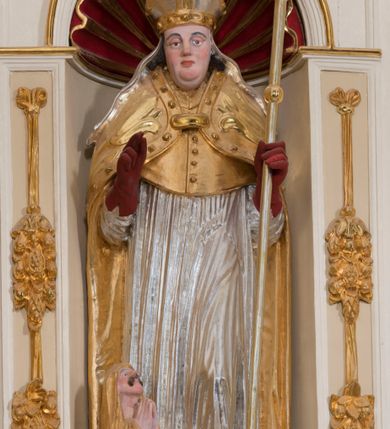 Zdjęcie nr 12: Ołtarz architektoniczny, dwukondygnacyjny, trójosiowy, ze zwieńczeniem. Ołtarz murowany, prostopadłościenny z marmurowym antepedium. Tabernakulum w formie prostopadłościennej, metalowej szafki ujętej parą ażurowych spływów wolutowych w formie stylizowanych wici akantowych. Drzwiczki, w kształcie zbliżonym do kwadratu, zdobione motywem krzyża i banderoli z napisem „IHS” ujętych kłosami zboża i kiściami winnej latorośli. Tron wystawienia w formie baldachimu wspartego na 4 kolumienkach. Krawędź zwieńczenia ujęta jest ornamentyką roślinną, w motywem kartusza z krzyżem po środku. Oś środkowa retabulum osadzona na wysokim, zdwojonym cokole o zryzalitowanych bokach. Pierwszą kondygnację ujmują dwie pary kolumn o kanelowanych trzonach i korynckich kapitelach, z czego wewnętrzne wysunięte względem lica nastawy, wspierających wyłamujące się ponad nimi belkowanie, w partii architrawu przybierające kształt  półkolistego łuku nadwieszonego; całość wieńczy forma trójkątnego przyczółka. Druga kondygnacja ujęta parą osadzonych na cokołach kolumn o trzonach zdobionych wicią winnej latorośli, wspierających delikatnie wyłamujące się ponad nimi belkowanie przerwane w partii fryzu u gzymsu. Zwieńczenie w formie trójkątnego, przerwanego przyczółka. W strefie zryzalitowanych po bokach cokołów osi bocznych para półkoliście zamkniętych bramek. Krawędzie zewnętrzne kondygnacji osi bocznych ujęte pojedynczymi kolumnami dźwigającymi wyłamujące się ponad nimi belkowanie wieńczące, będące przedłużeniem belkowania osi środkowej.  Pola cokołu retabulum wypełnione motywami ornamentyki roślinnej, w partii fryzu motywy małżowinowo-chrząstkowe. Druga kondygnacja osi środkowej ujęta parą ażurowych, małżowinowo-chrząstkowych uszaków, szczyt zwieńczenia w formie promienistej glorii z owalnym medalionem ujętym wieńcem obłoków, z monogramem imienia Jezus. Pola osi bocznych w dolnej partii zdobione motywami małżowinowo-chrząstkowego kartusza, w górnej owocowo-kwiatowymi festonami. Skrajne pola cokołu retabulum wypełnia para wizerunków – św. Pawła po prawej stronie i św. Piotra po lewej. Pole pierwszej kondygnacji osi środkowej ma formę płytkiej wnęki w kształcie stojącego prostokąta zamkniętego półkolistym łukiem nadwieszonym, ujętej bogato rzeźbioną ramą z motywem ornamentu małżowinowo-chrząstkowego, w środku obraz Matki Boskiej z Dzieciątkiem. Pole drugiej kondygnacji wypełnia obraz w kształcie leżącego prostokąta, ujęty szeroką ramą z uszakami w narożach, zdobioną ornamentem małżowinowo-chrząstkowym. Po bokach para półkoliście zamkniętych niszy z motywem konchy, wypełnionych parą figur – po prawej stronie św. Dominika, po lewej św. Antoni (?). Pola osi bocznych artykułuje para zamkniętych półkoliście niszy z motywami konchy, z parą rzeźb – św. Stanisława po prawej stronie i św. Wojciecha po lewej.  W szczycie osi bocznych pośrodku para rzeźb flankujących zwieńczenie ołtarza – po prawej stronie św. Wacława, po lewej św. Kazimierza, na końcach para figur aniołów. Struktura polichromowana w odcieniach koloru kremowego i beżowego, detal architektoniczny i ornamentyka złocone i srebrzone.