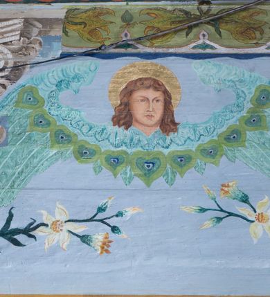 Zdjęcie nr 12: Ściany kościoła pokrywa dekoracja dywanowa, której w partiach stropu towarzyszą przedstawienia figuralne. W prezbiterium wykonano wyraźnie zaakcentowany fryz podstropowy, który od fasety oddziela profilowany i ornamentalnie malowany gzyms. Fryz na baldoniebieskim tle pokryto naprzemiennie rozmieszczonymi uskrzydlonymi główkami aniołów z niskimi wazonami z rozłożonymi trzema gałązkami kwitnących lilii. Poniżej barwnej bordiury oddzielającej fryz od pozostałych partii ścian, wykonano zgeometryzowaną dekorację utworzoną z powtarzających się wielobocznych pól, w których znalazł się stylizowany motyw tego samego kwiatu. Fasetę w prezbiterium pokryto naprzemiennie, rytmicznie rozmieszczonymi stylizowanymi kwiatami na łodydze i bez łodygi, które obwiedziono migdałowymi otokami tworzą ornamentalny pas zamknięty u góry falującą, wąską bordiurą. Dekorację bladoniebieskiego stropu prezbiterium tworzy poprowadzona przy krawędziach srebrno-niebieska arkatura. W centrum na niebieskim tle usianym złotymi gwiazdkami wyobrażono zasiadającą na obłokach Trójcę Świętą obramienioną pofalowaną, wielobarwną bordiurą otoczoną stylizowaną, srebrną wicią akantową. Dekoracyjną wić przedzielono parą uskrzydlonych główek anielskich oraz czterema stylizowanymi pąkami fantazyjnych kwiatów. Frontalnie ujęty Bóg Ojciec został wyobrażony jako siwobrody starzec o bujnych siwych włosach. W prawej ręce trzyma złote berło, lewą zaś wyciąga przed siebie. Bóg Ojciec prawą nogę opiera o niebieski glob, natomiast lewą, wyprostowaną wspiera się o obłoki. Jego twarz charakteryzuje jasna karnacja, szeroko otwarte oczy, wydatny nos i usta. Wokół głowy widać trójkąt. Obok Boga Ojca z lewej strony siedzi Chrystus, który obie nogi wspiera na globie. Zbawiciel trzymający oburącz na wysokości ramienia drewniany krzyż został przedstawiony w trzech czwartych w prawo. Jest to dojrzały mężczyzna o pociągłej twarzy okolonej brązowymi, długimi włosami spływającymi na ramiona oraz brodą. Ma jasną karnację, prosty nos i wydatne usta. Jego melancholijne spojrzenie jest skierowane w bok. Nagi tors okrywa bladoszkarłatny płaszcz odsłaniający prawą nogę. Na dłoniach i stopach widoczne są rany po gwoździach. Głowę Jezusa okala świetlisty nimb. Powyżej obu postaci unosi się gołębica Ducha Świętego w promienistym otoku. Niebieski glob na tle obłoków unoszą dwa aniołki w przepaskach. W nawie kościoła dekorację tworzą trzy różnej szerokości poziome pasy ornamentalne ułożone ponad jednolitą, szarą lamperią. Najszerszy pas pokryto na jasnym tle zgeometryzowanym ornamentem utworzonym z ciemnocynobrowych, migdałowo kształtowanych pól naśladujących wić roślinną. Powyżej rozmieszczono rytmicznie ułożone stylizowane krzyże równoramienne w fantazyjnych, wielobarwnych obramieniach. Najwyższy pas, odpowiadający fryzowi podstropowemu w prezbiterium pokryto wicią winnej latorośli z wplecionymi pękami kłosów. Tą część dekoracji zamyka profilowany gzyms ozdobiony wielobarwnym ornamentem zgeomertyzowanym. Rozpościerającą się ponad nim fasetę ozdobiono rytmicznie rozmieszczonym białym kwiatem na łodydze naśladujący w kształcie grzebień wodny. Dekorację bladoniebieskiego stropu artykułowano za pomocą srebrnej arkatury poprowadzonej przy jego krawędziach oraz ornamentalnych pasów utworzonych z motywów floralnych i geometrycznych, tworzących czworoboczną ramę dla centralnej kompozycji figuralnej. W narożach tego obramienia umieszczono medaliony ukazujące w popiersiach czterech ewangelistów malowanych na blasze miedzianej. Medaliony otaczają stylizowane gałązki dębowe z żołędziami. Każdego ewangelistę identyfikuje jego atrybut. W centrum stropu na bladozielonym tle usianym srebrnymi gwiazdkami namalowano wydłużone owalne obramienie utworzone z szerokiego wieńca różanego o bardzo drobnych kwiatach różanych i listkach. W jego centrum na tle bladoniebieskich obłoków ze złotymi gwiazdkami, bezpośrednio na deskach stropu, przedstawiono stojącą Madonnę z Dzieciątkiem, która depcze węża. Dodatkowo postać Marii zdaje się stać na rozpiętym różańcu. Maria ujęta frontalnie w kontrapoście obiema rękami podtrzymuje na prawym ramieniu Dzieciątko. Ma pociągłą twarz o jasnej karnacji, prostym nosie i wąskich ustach. Spojrzenie jej przymkniętych oczu jest skierowane w dół. Na głowie ma chustę szczelnie okrywającą jej włosy oraz złotą koronę o niskich sterczynach. Madonna ubrana jest w bladoczerwoną suknię odsłaniającą bosą stopę, którą depcze węża. Spod sukni na piersi widać białą koszulę. Na ramionach ma błękitny płaszcz podbity jasną ochrą, spięty na piersi podłużną, złotą klamrą. Trzymane przez nią Dzieciątko ma rozłożone ręce z uniesionymi dłońmi. Jego głowa ujęta jest w trzech czwartych w prawo. Otaczają ją jasno brązowe, krótkie włosy. Mały Jezus ubrany jest w jasną tunikę odsłaniającą jego bose stopy. Wokół Matki Boskiej rozmieszczono owalne medaliony z blachy miedzianej malowane w piętnaście tajemnic Różańca świętego. Ich narracja rozpoczyna się nad głową Madonny. Każda ze scen oparta jest o kilkuosobową kompozycję. Idąc w lewo namalowano: Zwiastowanie Marii, Nawiedzenie św. Elżbiety, Boże Narodzenie, Ofiarowanie w świątyni, Znalezienie w świątyni, Modlitwa w Ogrójcu, Biczowanie, Cierniem ukoronowanie, Niesienie krzyża, Ukrzyżowanie, Zmartwychwstanie, Wniebowstąpienie, Zesłanie Ducha Świętego, Wniebowzięcie Marii, Ukoronowanie Marii w niebie. Pomiędzy medalionami namalowano białą i czerwoną różę. Jasny parapet chóru muzycznego udekorowano naprzemiennie rozmieszczonymi rytmicznie stylizowanymi łodygami zakończonymi białymi pąkami i krzyżami równoramiennymi wpisanymi w koło. W aneksie południowym namalowano na ścianie kazanie św. Franciszka z Asyżu do ptaków. Kompozycja uzyskała kształt wydłużonego, stojącego prostokąta zamkniętego półkoliście i obwiedzionego falującą bordiurą z motywem łączących się krzyżyków. W jej centrum wyobrażono siedzącego na skalnym podłożu św. Franciszka ujętego w trzech czwartych w lewo. Święty prawą rękę unosi w geście mowy lewą zaś swobodnie trzyma na kolanach. Jego widoczną z profilu twarz o jasnej karnacji i prostym nosie okala siwiejąca broda i włosy z wyciętą tonsurą. Ubrany jest w brązowy habit przewiązany sznurem. Przed Franciszkiem przedstawiono stadko słuchających świetego ptaków. W prawym rogu kompozycji namalowano drewniane taczki. Z tyłu za świętym na tle skał rośnie drzewo. Inne drzewo wyobrażono z lewej strony, nieco z tyłu, na tle nieba pokrytego baldoniebieskimi obłokami. U góry z lewej strony na tle obłoków widać niewielką postać Madonny z Dzieciątkiem w typie Matki Boskiej Częstochowskiej.      