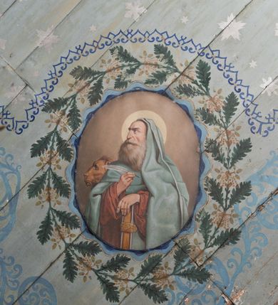 Zdjęcie nr 20: Ściany kościoła pokrywa dekoracja dywanowa, której w partiach stropu towarzyszą przedstawienia figuralne. W prezbiterium wykonano wyraźnie zaakcentowany fryz podstropowy, który od fasety oddziela profilowany i ornamentalnie malowany gzyms. Fryz na baldoniebieskim tle pokryto naprzemiennie rozmieszczonymi uskrzydlonymi główkami aniołów z niskimi wazonami z rozłożonymi trzema gałązkami kwitnących lilii. Poniżej barwnej bordiury oddzielającej fryz od pozostałych partii ścian, wykonano zgeometryzowaną dekorację utworzoną z powtarzających się wielobocznych pól, w których znalazł się stylizowany motyw tego samego kwiatu. Fasetę w prezbiterium pokryto naprzemiennie, rytmicznie rozmieszczonymi stylizowanymi kwiatami na łodydze i bez łodygi, które obwiedziono migdałowymi otokami tworzą ornamentalny pas zamknięty u góry falującą, wąską bordiurą. Dekorację bladoniebieskiego stropu prezbiterium tworzy poprowadzona przy krawędziach srebrno-niebieska arkatura. W centrum na niebieskim tle usianym złotymi gwiazdkami wyobrażono zasiadającą na obłokach Trójcę Świętą obramienioną pofalowaną, wielobarwną bordiurą otoczoną stylizowaną, srebrną wicią akantową. Dekoracyjną wić przedzielono parą uskrzydlonych główek anielskich oraz czterema stylizowanymi pąkami fantazyjnych kwiatów. Frontalnie ujęty Bóg Ojciec został wyobrażony jako siwobrody starzec o bujnych siwych włosach. W prawej ręce trzyma złote berło, lewą zaś wyciąga przed siebie. Bóg Ojciec prawą nogę opiera o niebieski glob, natomiast lewą, wyprostowaną wspiera się o obłoki. Jego twarz charakteryzuje jasna karnacja, szeroko otwarte oczy, wydatny nos i usta. Wokół głowy widać trójkąt. Obok Boga Ojca z lewej strony siedzi Chrystus, który obie nogi wspiera na globie. Zbawiciel trzymający oburącz na wysokości ramienia drewniany krzyż został przedstawiony w trzech czwartych w prawo. Jest to dojrzały mężczyzna o pociągłej twarzy okolonej brązowymi, długimi włosami spływającymi na ramiona oraz brodą. Ma jasną karnację, prosty nos i wydatne usta. Jego melancholijne spojrzenie jest skierowane w bok. Nagi tors okrywa bladoszkarłatny płaszcz odsłaniający prawą nogę. Na dłoniach i stopach widoczne są rany po gwoździach. Głowę Jezusa okala świetlisty nimb. Powyżej obu postaci unosi się gołębica Ducha Świętego w promienistym otoku. Niebieski glob na tle obłoków unoszą dwa aniołki w przepaskach. W nawie kościoła dekorację tworzą trzy różnej szerokości poziome pasy ornamentalne ułożone ponad jednolitą, szarą lamperią. Najszerszy pas pokryto na jasnym tle zgeometryzowanym ornamentem utworzonym z ciemnocynobrowych, migdałowo kształtowanych pól naśladujących wić roślinną. Powyżej rozmieszczono rytmicznie ułożone stylizowane krzyże równoramienne w fantazyjnych, wielobarwnych obramieniach. Najwyższy pas, odpowiadający fryzowi podstropowemu w prezbiterium pokryto wicią winnej latorośli z wplecionymi pękami kłosów. Tą część dekoracji zamyka profilowany gzyms ozdobiony wielobarwnym ornamentem zgeomertyzowanym. Rozpościerającą się ponad nim fasetę ozdobiono rytmicznie rozmieszczonym białym kwiatem na łodydze naśladujący w kształcie grzebień wodny. Dekorację bladoniebieskiego stropu artykułowano za pomocą srebrnej arkatury poprowadzonej przy jego krawędziach oraz ornamentalnych pasów utworzonych z motywów floralnych i geometrycznych, tworzących czworoboczną ramę dla centralnej kompozycji figuralnej. W narożach tego obramienia umieszczono medaliony ukazujące w popiersiach czterech ewangelistów malowanych na blasze miedzianej. Medaliony otaczają stylizowane gałązki dębowe z żołędziami. Każdego ewangelistę identyfikuje jego atrybut. W centrum stropu na bladozielonym tle usianym srebrnymi gwiazdkami namalowano wydłużone owalne obramienie utworzone z szerokiego wieńca różanego o bardzo drobnych kwiatach różanych i listkach. W jego centrum na tle bladoniebieskich obłoków ze złotymi gwiazdkami, bezpośrednio na deskach stropu, przedstawiono stojącą Madonnę z Dzieciątkiem, która depcze węża. Dodatkowo postać Marii zdaje się stać na rozpiętym różańcu. Maria ujęta frontalnie w kontrapoście obiema rękami podtrzymuje na prawym ramieniu Dzieciątko. Ma pociągłą twarz o jasnej karnacji, prostym nosie i wąskich ustach. Spojrzenie jej przymkniętych oczu jest skierowane w dół. Na głowie ma chustę szczelnie okrywającą jej włosy oraz złotą koronę o niskich sterczynach. Madonna ubrana jest w bladoczerwoną suknię odsłaniającą bosą stopę, którą depcze węża. Spod sukni na piersi widać białą koszulę. Na ramionach ma błękitny płaszcz podbity jasną ochrą, spięty na piersi podłużną, złotą klamrą. Trzymane przez nią Dzieciątko ma rozłożone ręce z uniesionymi dłońmi. Jego głowa ujęta jest w trzech czwartych w prawo. Otaczają ją jasno brązowe, krótkie włosy. Mały Jezus ubrany jest w jasną tunikę odsłaniającą jego bose stopy. Wokół Matki Boskiej rozmieszczono owalne medaliony z blachy miedzianej malowane w piętnaście tajemnic Różańca świętego. Ich narracja rozpoczyna się nad głową Madonny. Każda ze scen oparta jest o kilkuosobową kompozycję. Idąc w lewo namalowano: Zwiastowanie Marii, Nawiedzenie św. Elżbiety, Boże Narodzenie, Ofiarowanie w świątyni, Znalezienie w świątyni, Modlitwa w Ogrójcu, Biczowanie, Cierniem ukoronowanie, Niesienie krzyża, Ukrzyżowanie, Zmartwychwstanie, Wniebowstąpienie, Zesłanie Ducha Świętego, Wniebowzięcie Marii, Ukoronowanie Marii w niebie. Pomiędzy medalionami namalowano białą i czerwoną różę. Jasny parapet chóru muzycznego udekorowano naprzemiennie rozmieszczonymi rytmicznie stylizowanymi łodygami zakończonymi białymi pąkami i krzyżami równoramiennymi wpisanymi w koło. W aneksie południowym namalowano na ścianie kazanie św. Franciszka z Asyżu do ptaków. Kompozycja uzyskała kształt wydłużonego, stojącego prostokąta zamkniętego półkoliście i obwiedzionego falującą bordiurą z motywem łączących się krzyżyków. W jej centrum wyobrażono siedzącego na skalnym podłożu św. Franciszka ujętego w trzech czwartych w lewo. Święty prawą rękę unosi w geście mowy lewą zaś swobodnie trzyma na kolanach. Jego widoczną z profilu twarz o jasnej karnacji i prostym nosie okala siwiejąca broda i włosy z wyciętą tonsurą. Ubrany jest w brązowy habit przewiązany sznurem. Przed Franciszkiem przedstawiono stadko słuchających świetego ptaków. W prawym rogu kompozycji namalowano drewniane taczki. Z tyłu za świętym na tle skał rośnie drzewo. Inne drzewo wyobrażono z lewej strony, nieco z tyłu, na tle nieba pokrytego baldoniebieskimi obłokami. U góry z lewej strony na tle obłoków widać niewielką postać Madonny z Dzieciątkiem w typie Matki Boskiej Częstochowskiej.      
