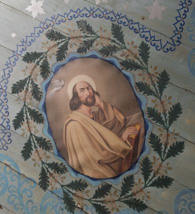 Zdjęcie nr 19: Ściany kościoła pokrywa dekoracja dywanowa, której w partiach stropu towarzyszą przedstawienia figuralne. W prezbiterium wykonano wyraźnie zaakcentowany fryz podstropowy, który od fasety oddziela profilowany i ornamentalnie malowany gzyms. Fryz na baldoniebieskim tle pokryto naprzemiennie rozmieszczonymi uskrzydlonymi główkami aniołów z niskimi wazonami z rozłożonymi trzema gałązkami kwitnących lilii. Poniżej barwnej bordiury oddzielającej fryz od pozostałych partii ścian, wykonano zgeometryzowaną dekorację utworzoną z powtarzających się wielobocznych pól, w których znalazł się stylizowany motyw tego samego kwiatu. Fasetę w prezbiterium pokryto naprzemiennie, rytmicznie rozmieszczonymi stylizowanymi kwiatami na łodydze i bez łodygi, które obwiedziono migdałowymi otokami tworzą ornamentalny pas zamknięty u góry falującą, wąską bordiurą. Dekorację bladoniebieskiego stropu prezbiterium tworzy poprowadzona przy krawędziach srebrno-niebieska arkatura. W centrum na niebieskim tle usianym złotymi gwiazdkami wyobrażono zasiadającą na obłokach Trójcę Świętą obramienioną pofalowaną, wielobarwną bordiurą otoczoną stylizowaną, srebrną wicią akantową. Dekoracyjną wić przedzielono parą uskrzydlonych główek anielskich oraz czterema stylizowanymi pąkami fantazyjnych kwiatów. Frontalnie ujęty Bóg Ojciec został wyobrażony jako siwobrody starzec o bujnych siwych włosach. W prawej ręce trzyma złote berło, lewą zaś wyciąga przed siebie. Bóg Ojciec prawą nogę opiera o niebieski glob, natomiast lewą, wyprostowaną wspiera się o obłoki. Jego twarz charakteryzuje jasna karnacja, szeroko otwarte oczy, wydatny nos i usta. Wokół głowy widać trójkąt. Obok Boga Ojca z lewej strony siedzi Chrystus, który obie nogi wspiera na globie. Zbawiciel trzymający oburącz na wysokości ramienia drewniany krzyż został przedstawiony w trzech czwartych w prawo. Jest to dojrzały mężczyzna o pociągłej twarzy okolonej brązowymi, długimi włosami spływającymi na ramiona oraz brodą. Ma jasną karnację, prosty nos i wydatne usta. Jego melancholijne spojrzenie jest skierowane w bok. Nagi tors okrywa bladoszkarłatny płaszcz odsłaniający prawą nogę. Na dłoniach i stopach widoczne są rany po gwoździach. Głowę Jezusa okala świetlisty nimb. Powyżej obu postaci unosi się gołębica Ducha Świętego w promienistym otoku. Niebieski glob na tle obłoków unoszą dwa aniołki w przepaskach. W nawie kościoła dekorację tworzą trzy różnej szerokości poziome pasy ornamentalne ułożone ponad jednolitą, szarą lamperią. Najszerszy pas pokryto na jasnym tle zgeometryzowanym ornamentem utworzonym z ciemnocynobrowych, migdałowo kształtowanych pól naśladujących wić roślinną. Powyżej rozmieszczono rytmicznie ułożone stylizowane krzyże równoramienne w fantazyjnych, wielobarwnych obramieniach. Najwyższy pas, odpowiadający fryzowi podstropowemu w prezbiterium pokryto wicią winnej latorośli z wplecionymi pękami kłosów. Tą część dekoracji zamyka profilowany gzyms ozdobiony wielobarwnym ornamentem zgeomertyzowanym. Rozpościerającą się ponad nim fasetę ozdobiono rytmicznie rozmieszczonym białym kwiatem na łodydze naśladujący w kształcie grzebień wodny. Dekorację bladoniebieskiego stropu artykułowano za pomocą srebrnej arkatury poprowadzonej przy jego krawędziach oraz ornamentalnych pasów utworzonych z motywów floralnych i geometrycznych, tworzących czworoboczną ramę dla centralnej kompozycji figuralnej. W narożach tego obramienia umieszczono medaliony ukazujące w popiersiach czterech ewangelistów malowanych na blasze miedzianej. Medaliony otaczają stylizowane gałązki dębowe z żołędziami. Każdego ewangelistę identyfikuje jego atrybut. W centrum stropu na bladozielonym tle usianym srebrnymi gwiazdkami namalowano wydłużone owalne obramienie utworzone z szerokiego wieńca różanego o bardzo drobnych kwiatach różanych i listkach. W jego centrum na tle bladoniebieskich obłoków ze złotymi gwiazdkami, bezpośrednio na deskach stropu, przedstawiono stojącą Madonnę z Dzieciątkiem, która depcze węża. Dodatkowo postać Marii zdaje się stać na rozpiętym różańcu. Maria ujęta frontalnie w kontrapoście obiema rękami podtrzymuje na prawym ramieniu Dzieciątko. Ma pociągłą twarz o jasnej karnacji, prostym nosie i wąskich ustach. Spojrzenie jej przymkniętych oczu jest skierowane w dół. Na głowie ma chustę szczelnie okrywającą jej włosy oraz złotą koronę o niskich sterczynach. Madonna ubrana jest w bladoczerwoną suknię odsłaniającą bosą stopę, którą depcze węża. Spod sukni na piersi widać białą koszulę. Na ramionach ma błękitny płaszcz podbity jasną ochrą, spięty na piersi podłużną, złotą klamrą. Trzymane przez nią Dzieciątko ma rozłożone ręce z uniesionymi dłońmi. Jego głowa ujęta jest w trzech czwartych w prawo. Otaczają ją jasno brązowe, krótkie włosy. Mały Jezus ubrany jest w jasną tunikę odsłaniającą jego bose stopy. Wokół Matki Boskiej rozmieszczono owalne medaliony z blachy miedzianej malowane w piętnaście tajemnic Różańca świętego. Ich narracja rozpoczyna się nad głową Madonny. Każda ze scen oparta jest o kilkuosobową kompozycję. Idąc w lewo namalowano: Zwiastowanie Marii, Nawiedzenie św. Elżbiety, Boże Narodzenie, Ofiarowanie w świątyni, Znalezienie w świątyni, Modlitwa w Ogrójcu, Biczowanie, Cierniem ukoronowanie, Niesienie krzyża, Ukrzyżowanie, Zmartwychwstanie, Wniebowstąpienie, Zesłanie Ducha Świętego, Wniebowzięcie Marii, Ukoronowanie Marii w niebie. Pomiędzy medalionami namalowano białą i czerwoną różę. Jasny parapet chóru muzycznego udekorowano naprzemiennie rozmieszczonymi rytmicznie stylizowanymi łodygami zakończonymi białymi pąkami i krzyżami równoramiennymi wpisanymi w koło. W aneksie południowym namalowano na ścianie kazanie św. Franciszka z Asyżu do ptaków. Kompozycja uzyskała kształt wydłużonego, stojącego prostokąta zamkniętego półkoliście i obwiedzionego falującą bordiurą z motywem łączących się krzyżyków. W jej centrum wyobrażono siedzącego na skalnym podłożu św. Franciszka ujętego w trzech czwartych w lewo. Święty prawą rękę unosi w geście mowy lewą zaś swobodnie trzyma na kolanach. Jego widoczną z profilu twarz o jasnej karnacji i prostym nosie okala siwiejąca broda i włosy z wyciętą tonsurą. Ubrany jest w brązowy habit przewiązany sznurem. Przed Franciszkiem przedstawiono stadko słuchających świetego ptaków. W prawym rogu kompozycji namalowano drewniane taczki. Z tyłu za świętym na tle skał rośnie drzewo. Inne drzewo wyobrażono z lewej strony, nieco z tyłu, na tle nieba pokrytego baldoniebieskimi obłokami. U góry z lewej strony na tle obłoków widać niewielką postać Madonny z Dzieciątkiem w typie Matki Boskiej Częstochowskiej.      