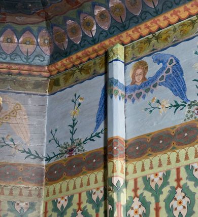 Zdjęcie nr 11: Ściany kościoła pokrywa dekoracja dywanowa, której w partiach stropu towarzyszą przedstawienia figuralne. W prezbiterium wykonano wyraźnie zaakcentowany fryz podstropowy, który od fasety oddziela profilowany i ornamentalnie malowany gzyms. Fryz na baldoniebieskim tle pokryto naprzemiennie rozmieszczonymi uskrzydlonymi główkami aniołów z niskimi wazonami z rozłożonymi trzema gałązkami kwitnących lilii. Poniżej barwnej bordiury oddzielającej fryz od pozostałych partii ścian, wykonano zgeometryzowaną dekorację utworzoną z powtarzających się wielobocznych pól, w których znalazł się stylizowany motyw tego samego kwiatu. Fasetę w prezbiterium pokryto naprzemiennie, rytmicznie rozmieszczonymi stylizowanymi kwiatami na łodydze i bez łodygi, które obwiedziono migdałowymi otokami tworzą ornamentalny pas zamknięty u góry falującą, wąską bordiurą. Dekorację bladoniebieskiego stropu prezbiterium tworzy poprowadzona przy krawędziach srebrno-niebieska arkatura. W centrum na niebieskim tle usianym złotymi gwiazdkami wyobrażono zasiadającą na obłokach Trójcę Świętą obramienioną pofalowaną, wielobarwną bordiurą otoczoną stylizowaną, srebrną wicią akantową. Dekoracyjną wić przedzielono parą uskrzydlonych główek anielskich oraz czterema stylizowanymi pąkami fantazyjnych kwiatów. Frontalnie ujęty Bóg Ojciec został wyobrażony jako siwobrody starzec o bujnych siwych włosach. W prawej ręce trzyma złote berło, lewą zaś wyciąga przed siebie. Bóg Ojciec prawą nogę opiera o niebieski glob, natomiast lewą, wyprostowaną wspiera się o obłoki. Jego twarz charakteryzuje jasna karnacja, szeroko otwarte oczy, wydatny nos i usta. Wokół głowy widać trójkąt. Obok Boga Ojca z lewej strony siedzi Chrystus, który obie nogi wspiera na globie. Zbawiciel trzymający oburącz na wysokości ramienia drewniany krzyż został przedstawiony w trzech czwartych w prawo. Jest to dojrzały mężczyzna o pociągłej twarzy okolonej brązowymi, długimi włosami spływającymi na ramiona oraz brodą. Ma jasną karnację, prosty nos i wydatne usta. Jego melancholijne spojrzenie jest skierowane w bok. Nagi tors okrywa bladoszkarłatny płaszcz odsłaniający prawą nogę. Na dłoniach i stopach widoczne są rany po gwoździach. Głowę Jezusa okala świetlisty nimb. Powyżej obu postaci unosi się gołębica Ducha Świętego w promienistym otoku. Niebieski glob na tle obłoków unoszą dwa aniołki w przepaskach. W nawie kościoła dekorację tworzą trzy różnej szerokości poziome pasy ornamentalne ułożone ponad jednolitą, szarą lamperią. Najszerszy pas pokryto na jasnym tle zgeometryzowanym ornamentem utworzonym z ciemnocynobrowych, migdałowo kształtowanych pól naśladujących wić roślinną. Powyżej rozmieszczono rytmicznie ułożone stylizowane krzyże równoramienne w fantazyjnych, wielobarwnych obramieniach. Najwyższy pas, odpowiadający fryzowi podstropowemu w prezbiterium pokryto wicią winnej latorośli z wplecionymi pękami kłosów. Tą część dekoracji zamyka profilowany gzyms ozdobiony wielobarwnym ornamentem zgeomertyzowanym. Rozpościerającą się ponad nim fasetę ozdobiono rytmicznie rozmieszczonym białym kwiatem na łodydze naśladujący w kształcie grzebień wodny. Dekorację bladoniebieskiego stropu artykułowano za pomocą srebrnej arkatury poprowadzonej przy jego krawędziach oraz ornamentalnych pasów utworzonych z motywów floralnych i geometrycznych, tworzących czworoboczną ramę dla centralnej kompozycji figuralnej. W narożach tego obramienia umieszczono medaliony ukazujące w popiersiach czterech ewangelistów malowanych na blasze miedzianej. Medaliony otaczają stylizowane gałązki dębowe z żołędziami. Każdego ewangelistę identyfikuje jego atrybut. W centrum stropu na bladozielonym tle usianym srebrnymi gwiazdkami namalowano wydłużone owalne obramienie utworzone z szerokiego wieńca różanego o bardzo drobnych kwiatach różanych i listkach. W jego centrum na tle bladoniebieskich obłoków ze złotymi gwiazdkami, bezpośrednio na deskach stropu, przedstawiono stojącą Madonnę z Dzieciątkiem, która depcze węża. Dodatkowo postać Marii zdaje się stać na rozpiętym różańcu. Maria ujęta frontalnie w kontrapoście obiema rękami podtrzymuje na prawym ramieniu Dzieciątko. Ma pociągłą twarz o jasnej karnacji, prostym nosie i wąskich ustach. Spojrzenie jej przymkniętych oczu jest skierowane w dół. Na głowie ma chustę szczelnie okrywającą jej włosy oraz złotą koronę o niskich sterczynach. Madonna ubrana jest w bladoczerwoną suknię odsłaniającą bosą stopę, którą depcze węża. Spod sukni na piersi widać białą koszulę. Na ramionach ma błękitny płaszcz podbity jasną ochrą, spięty na piersi podłużną, złotą klamrą. Trzymane przez nią Dzieciątko ma rozłożone ręce z uniesionymi dłońmi. Jego głowa ujęta jest w trzech czwartych w prawo. Otaczają ją jasno brązowe, krótkie włosy. Mały Jezus ubrany jest w jasną tunikę odsłaniającą jego bose stopy. Wokół Matki Boskiej rozmieszczono owalne medaliony z blachy miedzianej malowane w piętnaście tajemnic Różańca świętego. Ich narracja rozpoczyna się nad głową Madonny. Każda ze scen oparta jest o kilkuosobową kompozycję. Idąc w lewo namalowano: Zwiastowanie Marii, Nawiedzenie św. Elżbiety, Boże Narodzenie, Ofiarowanie w świątyni, Znalezienie w świątyni, Modlitwa w Ogrójcu, Biczowanie, Cierniem ukoronowanie, Niesienie krzyża, Ukrzyżowanie, Zmartwychwstanie, Wniebowstąpienie, Zesłanie Ducha Świętego, Wniebowzięcie Marii, Ukoronowanie Marii w niebie. Pomiędzy medalionami namalowano białą i czerwoną różę. Jasny parapet chóru muzycznego udekorowano naprzemiennie rozmieszczonymi rytmicznie stylizowanymi łodygami zakończonymi białymi pąkami i krzyżami równoramiennymi wpisanymi w koło. W aneksie południowym namalowano na ścianie kazanie św. Franciszka z Asyżu do ptaków. Kompozycja uzyskała kształt wydłużonego, stojącego prostokąta zamkniętego półkoliście i obwiedzionego falującą bordiurą z motywem łączących się krzyżyków. W jej centrum wyobrażono siedzącego na skalnym podłożu św. Franciszka ujętego w trzech czwartych w lewo. Święty prawą rękę unosi w geście mowy lewą zaś swobodnie trzyma na kolanach. Jego widoczną z profilu twarz o jasnej karnacji i prostym nosie okala siwiejąca broda i włosy z wyciętą tonsurą. Ubrany jest w brązowy habit przewiązany sznurem. Przed Franciszkiem przedstawiono stadko słuchających świetego ptaków. W prawym rogu kompozycji namalowano drewniane taczki. Z tyłu za świętym na tle skał rośnie drzewo. Inne drzewo wyobrażono z lewej strony, nieco z tyłu, na tle nieba pokrytego baldoniebieskimi obłokami. U góry z lewej strony na tle obłoków widać niewielką postać Madonny z Dzieciątkiem w typie Matki Boskiej Częstochowskiej.      