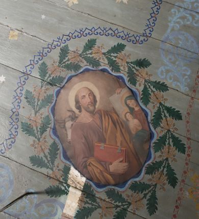 Zdjęcie nr 21: Ściany kościoła pokrywa dekoracja dywanowa, której w partiach stropu towarzyszą przedstawienia figuralne. W prezbiterium wykonano wyraźnie zaakcentowany fryz podstropowy, który od fasety oddziela profilowany i ornamentalnie malowany gzyms. Fryz na baldoniebieskim tle pokryto naprzemiennie rozmieszczonymi uskrzydlonymi główkami aniołów z niskimi wazonami z rozłożonymi trzema gałązkami kwitnących lilii. Poniżej barwnej bordiury oddzielającej fryz od pozostałych partii ścian, wykonano zgeometryzowaną dekorację utworzoną z powtarzających się wielobocznych pól, w których znalazł się stylizowany motyw tego samego kwiatu. Fasetę w prezbiterium pokryto naprzemiennie, rytmicznie rozmieszczonymi stylizowanymi kwiatami na łodydze i bez łodygi, które obwiedziono migdałowymi otokami tworzą ornamentalny pas zamknięty u góry falującą, wąską bordiurą. Dekorację bladoniebieskiego stropu prezbiterium tworzy poprowadzona przy krawędziach srebrno-niebieska arkatura. W centrum na niebieskim tle usianym złotymi gwiazdkami wyobrażono zasiadającą na obłokach Trójcę Świętą obramienioną pofalowaną, wielobarwną bordiurą otoczoną stylizowaną, srebrną wicią akantową. Dekoracyjną wić przedzielono parą uskrzydlonych główek anielskich oraz czterema stylizowanymi pąkami fantazyjnych kwiatów. Frontalnie ujęty Bóg Ojciec został wyobrażony jako siwobrody starzec o bujnych siwych włosach. W prawej ręce trzyma złote berło, lewą zaś wyciąga przed siebie. Bóg Ojciec prawą nogę opiera o niebieski glob, natomiast lewą, wyprostowaną wspiera się o obłoki. Jego twarz charakteryzuje jasna karnacja, szeroko otwarte oczy, wydatny nos i usta. Wokół głowy widać trójkąt. Obok Boga Ojca z lewej strony siedzi Chrystus, który obie nogi wspiera na globie. Zbawiciel trzymający oburącz na wysokości ramienia drewniany krzyż został przedstawiony w trzech czwartych w prawo. Jest to dojrzały mężczyzna o pociągłej twarzy okolonej brązowymi, długimi włosami spływającymi na ramiona oraz brodą. Ma jasną karnację, prosty nos i wydatne usta. Jego melancholijne spojrzenie jest skierowane w bok. Nagi tors okrywa bladoszkarłatny płaszcz odsłaniający prawą nogę. Na dłoniach i stopach widoczne są rany po gwoździach. Głowę Jezusa okala świetlisty nimb. Powyżej obu postaci unosi się gołębica Ducha Świętego w promienistym otoku. Niebieski glob na tle obłoków unoszą dwa aniołki w przepaskach. W nawie kościoła dekorację tworzą trzy różnej szerokości poziome pasy ornamentalne ułożone ponad jednolitą, szarą lamperią. Najszerszy pas pokryto na jasnym tle zgeometryzowanym ornamentem utworzonym z ciemnocynobrowych, migdałowo kształtowanych pól naśladujących wić roślinną. Powyżej rozmieszczono rytmicznie ułożone stylizowane krzyże równoramienne w fantazyjnych, wielobarwnych obramieniach. Najwyższy pas, odpowiadający fryzowi podstropowemu w prezbiterium pokryto wicią winnej latorośli z wplecionymi pękami kłosów. Tą część dekoracji zamyka profilowany gzyms ozdobiony wielobarwnym ornamentem zgeomertyzowanym. Rozpościerającą się ponad nim fasetę ozdobiono rytmicznie rozmieszczonym białym kwiatem na łodydze naśladujący w kształcie grzebień wodny. Dekorację bladoniebieskiego stropu artykułowano za pomocą srebrnej arkatury poprowadzonej przy jego krawędziach oraz ornamentalnych pasów utworzonych z motywów floralnych i geometrycznych, tworzących czworoboczną ramę dla centralnej kompozycji figuralnej. W narożach tego obramienia umieszczono medaliony ukazujące w popiersiach czterech ewangelistów malowanych na blasze miedzianej. Medaliony otaczają stylizowane gałązki dębowe z żołędziami. Każdego ewangelistę identyfikuje jego atrybut. W centrum stropu na bladozielonym tle usianym srebrnymi gwiazdkami namalowano wydłużone owalne obramienie utworzone z szerokiego wieńca różanego o bardzo drobnych kwiatach różanych i listkach. W jego centrum na tle bladoniebieskich obłoków ze złotymi gwiazdkami, bezpośrednio na deskach stropu, przedstawiono stojącą Madonnę z Dzieciątkiem, która depcze węża. Dodatkowo postać Marii zdaje się stać na rozpiętym różańcu. Maria ujęta frontalnie w kontrapoście obiema rękami podtrzymuje na prawym ramieniu Dzieciątko. Ma pociągłą twarz o jasnej karnacji, prostym nosie i wąskich ustach. Spojrzenie jej przymkniętych oczu jest skierowane w dół. Na głowie ma chustę szczelnie okrywającą jej włosy oraz złotą koronę o niskich sterczynach. Madonna ubrana jest w bladoczerwoną suknię odsłaniającą bosą stopę, którą depcze węża. Spod sukni na piersi widać białą koszulę. Na ramionach ma błękitny płaszcz podbity jasną ochrą, spięty na piersi podłużną, złotą klamrą. Trzymane przez nią Dzieciątko ma rozłożone ręce z uniesionymi dłońmi. Jego głowa ujęta jest w trzech czwartych w prawo. Otaczają ją jasno brązowe, krótkie włosy. Mały Jezus ubrany jest w jasną tunikę odsłaniającą jego bose stopy. Wokół Matki Boskiej rozmieszczono owalne medaliony z blachy miedzianej malowane w piętnaście tajemnic Różańca świętego. Ich narracja rozpoczyna się nad głową Madonny. Każda ze scen oparta jest o kilkuosobową kompozycję. Idąc w lewo namalowano: Zwiastowanie Marii, Nawiedzenie św. Elżbiety, Boże Narodzenie, Ofiarowanie w świątyni, Znalezienie w świątyni, Modlitwa w Ogrójcu, Biczowanie, Cierniem ukoronowanie, Niesienie krzyża, Ukrzyżowanie, Zmartwychwstanie, Wniebowstąpienie, Zesłanie Ducha Świętego, Wniebowzięcie Marii, Ukoronowanie Marii w niebie. Pomiędzy medalionami namalowano białą i czerwoną różę. Jasny parapet chóru muzycznego udekorowano naprzemiennie rozmieszczonymi rytmicznie stylizowanymi łodygami zakończonymi białymi pąkami i krzyżami równoramiennymi wpisanymi w koło. W aneksie południowym namalowano na ścianie kazanie św. Franciszka z Asyżu do ptaków. Kompozycja uzyskała kształt wydłużonego, stojącego prostokąta zamkniętego półkoliście i obwiedzionego falującą bordiurą z motywem łączących się krzyżyków. W jej centrum wyobrażono siedzącego na skalnym podłożu św. Franciszka ujętego w trzech czwartych w lewo. Święty prawą rękę unosi w geście mowy lewą zaś swobodnie trzyma na kolanach. Jego widoczną z profilu twarz o jasnej karnacji i prostym nosie okala siwiejąca broda i włosy z wyciętą tonsurą. Ubrany jest w brązowy habit przewiązany sznurem. Przed Franciszkiem przedstawiono stadko słuchających świetego ptaków. W prawym rogu kompozycji namalowano drewniane taczki. Z tyłu za świętym na tle skał rośnie drzewo. Inne drzewo wyobrażono z lewej strony, nieco z tyłu, na tle nieba pokrytego baldoniebieskimi obłokami. U góry z lewej strony na tle obłoków widać niewielką postać Madonny z Dzieciątkiem w typie Matki Boskiej Częstochowskiej.      