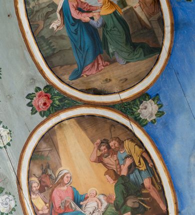 Zdjęcie nr 24: Ściany kościoła pokrywa dekoracja dywanowa, której w partiach stropu towarzyszą przedstawienia figuralne. W prezbiterium wykonano wyraźnie zaakcentowany fryz podstropowy, który od fasety oddziela profilowany i ornamentalnie malowany gzyms. Fryz na baldoniebieskim tle pokryto naprzemiennie rozmieszczonymi uskrzydlonymi główkami aniołów z niskimi wazonami z rozłożonymi trzema gałązkami kwitnących lilii. Poniżej barwnej bordiury oddzielającej fryz od pozostałych partii ścian, wykonano zgeometryzowaną dekorację utworzoną z powtarzających się wielobocznych pól, w których znalazł się stylizowany motyw tego samego kwiatu. Fasetę w prezbiterium pokryto naprzemiennie, rytmicznie rozmieszczonymi stylizowanymi kwiatami na łodydze i bez łodygi, które obwiedziono migdałowymi otokami tworzą ornamentalny pas zamknięty u góry falującą, wąską bordiurą. Dekorację bladoniebieskiego stropu prezbiterium tworzy poprowadzona przy krawędziach srebrno-niebieska arkatura. W centrum na niebieskim tle usianym złotymi gwiazdkami wyobrażono zasiadającą na obłokach Trójcę Świętą obramienioną pofalowaną, wielobarwną bordiurą otoczoną stylizowaną, srebrną wicią akantową. Dekoracyjną wić przedzielono parą uskrzydlonych główek anielskich oraz czterema stylizowanymi pąkami fantazyjnych kwiatów. Frontalnie ujęty Bóg Ojciec został wyobrażony jako siwobrody starzec o bujnych siwych włosach. W prawej ręce trzyma złote berło, lewą zaś wyciąga przed siebie. Bóg Ojciec prawą nogę opiera o niebieski glob, natomiast lewą, wyprostowaną wspiera się o obłoki. Jego twarz charakteryzuje jasna karnacja, szeroko otwarte oczy, wydatny nos i usta. Wokół głowy widać trójkąt. Obok Boga Ojca z lewej strony siedzi Chrystus, który obie nogi wspiera na globie. Zbawiciel trzymający oburącz na wysokości ramienia drewniany krzyż został przedstawiony w trzech czwartych w prawo. Jest to dojrzały mężczyzna o pociągłej twarzy okolonej brązowymi, długimi włosami spływającymi na ramiona oraz brodą. Ma jasną karnację, prosty nos i wydatne usta. Jego melancholijne spojrzenie jest skierowane w bok. Nagi tors okrywa bladoszkarłatny płaszcz odsłaniający prawą nogę. Na dłoniach i stopach widoczne są rany po gwoździach. Głowę Jezusa okala świetlisty nimb. Powyżej obu postaci unosi się gołębica Ducha Świętego w promienistym otoku. Niebieski glob na tle obłoków unoszą dwa aniołki w przepaskach. W nawie kościoła dekorację tworzą trzy różnej szerokości poziome pasy ornamentalne ułożone ponad jednolitą, szarą lamperią. Najszerszy pas pokryto na jasnym tle zgeometryzowanym ornamentem utworzonym z ciemnocynobrowych, migdałowo kształtowanych pól naśladujących wić roślinną. Powyżej rozmieszczono rytmicznie ułożone stylizowane krzyże równoramienne w fantazyjnych, wielobarwnych obramieniach. Najwyższy pas, odpowiadający fryzowi podstropowemu w prezbiterium pokryto wicią winnej latorośli z wplecionymi pękami kłosów. Tą część dekoracji zamyka profilowany gzyms ozdobiony wielobarwnym ornamentem zgeomertyzowanym. Rozpościerającą się ponad nim fasetę ozdobiono rytmicznie rozmieszczonym białym kwiatem na łodydze naśladujący w kształcie grzebień wodny. Dekorację bladoniebieskiego stropu artykułowano za pomocą srebrnej arkatury poprowadzonej przy jego krawędziach oraz ornamentalnych pasów utworzonych z motywów floralnych i geometrycznych, tworzących czworoboczną ramę dla centralnej kompozycji figuralnej. W narożach tego obramienia umieszczono medaliony ukazujące w popiersiach czterech ewangelistów malowanych na blasze miedzianej. Medaliony otaczają stylizowane gałązki dębowe z żołędziami. Każdego ewangelistę identyfikuje jego atrybut. W centrum stropu na bladozielonym tle usianym srebrnymi gwiazdkami namalowano wydłużone owalne obramienie utworzone z szerokiego wieńca różanego o bardzo drobnych kwiatach różanych i listkach. W jego centrum na tle bladoniebieskich obłoków ze złotymi gwiazdkami, bezpośrednio na deskach stropu, przedstawiono stojącą Madonnę z Dzieciątkiem, która depcze węża. Dodatkowo postać Marii zdaje się stać na rozpiętym różańcu. Maria ujęta frontalnie w kontrapoście obiema rękami podtrzymuje na prawym ramieniu Dzieciątko. Ma pociągłą twarz o jasnej karnacji, prostym nosie i wąskich ustach. Spojrzenie jej przymkniętych oczu jest skierowane w dół. Na głowie ma chustę szczelnie okrywającą jej włosy oraz złotą koronę o niskich sterczynach. Madonna ubrana jest w bladoczerwoną suknię odsłaniającą bosą stopę, którą depcze węża. Spod sukni na piersi widać białą koszulę. Na ramionach ma błękitny płaszcz podbity jasną ochrą, spięty na piersi podłużną, złotą klamrą. Trzymane przez nią Dzieciątko ma rozłożone ręce z uniesionymi dłońmi. Jego głowa ujęta jest w trzech czwartych w prawo. Otaczają ją jasno brązowe, krótkie włosy. Mały Jezus ubrany jest w jasną tunikę odsłaniającą jego bose stopy. Wokół Matki Boskiej rozmieszczono owalne medaliony z blachy miedzianej malowane w piętnaście tajemnic Różańca świętego. Ich narracja rozpoczyna się nad głową Madonny. Każda ze scen oparta jest o kilkuosobową kompozycję. Idąc w lewo namalowano: Zwiastowanie Marii, Nawiedzenie św. Elżbiety, Boże Narodzenie, Ofiarowanie w świątyni, Znalezienie w świątyni, Modlitwa w Ogrójcu, Biczowanie, Cierniem ukoronowanie, Niesienie krzyża, Ukrzyżowanie, Zmartwychwstanie, Wniebowstąpienie, Zesłanie Ducha Świętego, Wniebowzięcie Marii, Ukoronowanie Marii w niebie. Pomiędzy medalionami namalowano białą i czerwoną różę. Jasny parapet chóru muzycznego udekorowano naprzemiennie rozmieszczonymi rytmicznie stylizowanymi łodygami zakończonymi białymi pąkami i krzyżami równoramiennymi wpisanymi w koło. W aneksie południowym namalowano na ścianie kazanie św. Franciszka z Asyżu do ptaków. Kompozycja uzyskała kształt wydłużonego, stojącego prostokąta zamkniętego półkoliście i obwiedzionego falującą bordiurą z motywem łączących się krzyżyków. W jej centrum wyobrażono siedzącego na skalnym podłożu św. Franciszka ujętego w trzech czwartych w lewo. Święty prawą rękę unosi w geście mowy lewą zaś swobodnie trzyma na kolanach. Jego widoczną z profilu twarz o jasnej karnacji i prostym nosie okala siwiejąca broda i włosy z wyciętą tonsurą. Ubrany jest w brązowy habit przewiązany sznurem. Przed Franciszkiem przedstawiono stadko słuchających świetego ptaków. W prawym rogu kompozycji namalowano drewniane taczki. Z tyłu za świętym na tle skał rośnie drzewo. Inne drzewo wyobrażono z lewej strony, nieco z tyłu, na tle nieba pokrytego baldoniebieskimi obłokami. U góry z lewej strony na tle obłoków widać niewielką postać Madonny z Dzieciątkiem w typie Matki Boskiej Częstochowskiej.      