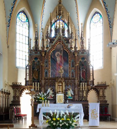 Zdjęcie nr 1: Drewniany ołtarz główny w Osieku uzyskał formę przyściennej, jednokondygnacyjnej, architektonicznej struktury trójosiowej z bramkami. Drewniana mensa z portatylem wspiera się na prostopadłościennym stipesie ołtarzowym. Jego fronton artykułują kolumienki o gładkich trzonach i złoconych podstawach oraz kapitelach z „gotyckim” akantem. Pomiędzy nimi w polach usytuowano złocone płyciny w kształcie leżącego prostokąta zamkniętego łukiem trójlistnym ściętym. Wypełniono je płaskorzeźbionymi, polichromowanymi przedstawieniami ofiary Abrahama, Ostatniej Wieczerzy oraz ofiary Melchizedeka. Na mensie ustawiono prostopadłościenne tabernakulum pancerne z tronem wystawienia w formie oktagonalnej kapliczki ujętej ustawionymi ukośnie kolumienkami o skręconych trzonach zwieńczonej wimpergami, wypełnionymi złoconym „gotyckim” akantem oraz pinaklami. Na podniebiu baldachimu wyobrażono gołębicę Ducha Świętego na tle glorii promienistej oraz lilie heraldyczne w ukośnej kratownicy. Tron wystawienia ujęty został polichromowanymi postaciami klęczących aniołów, ponad którymi rozpięto ostrołukowy baldachim z wimpergami i pinaklami wsparty na gotyckich półkolumienkach. Samo retabulum ustawiono na wysokim dwukondygnacyjnym cokole artykułowanym w pierwszej kondygnacji wąskimi, ostołukowymi płycinami wypełnionymi dekoracją pseudomaswerkową. Natomiast na drugim poziomie znalazły się gotyckie kolumienki na wysokich cokołach dźwigające przecinające się łuki wypełnione dekoracją pseudomaswerkową w formie trójliści. W polach pomiędzy kolumienkami zastosowano symetryczny ornament utworzony z gotyckiego akantu, płaskorzeźbione i złocone przedstawienia aniołów, winne grona, kłosy oraz czwórliście. Wznoszącą się na cokole nastawę artykułowano „gotyckimi” kolumnami o gładkich trzonach i złoconych korynckich kapitelach. Dodatkowo w osi środkowej kolumny w połowie wysokości ozdobiono akantowymi talerzykami. Pole środkowe retabulum uzyskało kształt stojącego prostokąta zamkniętego łukiem trójlistnym, w którym zainstalowano figurę Chrystusa Bolesnego, a na zasuwach obraz św. Andrzeja oraz obraz Matki Boskiej Niepokalanie Poczętej. Ujmuje je profilowane, złocone obramienie zamknięte ostrołukową wimpergą ujęty po bokach dwoma kondygnacjami zamkniętych trójlistnie nisz mieszczących polichromowane figury: św. Łukasza, św. Jana Ewangelisty, św. Mateusza i św. Marka. W osiach bocznych nastawy ustawiono w niszach zamkniętych trójlistnie polichromowane figury św. Piotra i św. Pawła na tle malowanego astwerku oraz złotych gwiazd w podniebiu. Rozbudowane, ażurowe zwieńczenie ołtarza uzyskało formę licznych pinakli dekorowanych złoconymi czołgankami, otaczającymi ażurową edikulę zwieńczoną krzyżem. Dodatkowo w osi środkowej ustawiono polichromowane figury aniołów trzymających banderole. Bramki ołtarzowe uzyskały formę ostrołukowych przejść dekorowanych rzeźbionym maswerskiem z motywami trójliścia. Całą struktura nastawy jest bejcowana i lakierowana w kolorze ciemnego brązu.Natomiast załamania profili architektonicznych malowane zostały na czerwono i błękitno. Płaskorzeźbione ornamenty pozłocone, zaś figury otrzymały pełne polichromowanie.