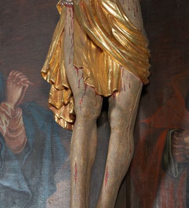 Zdjęcie nr 7: Krucyfiks w typie Christo morte; postać  Chrystusa umarłego przybitego do krzyża trzema gwoździami. Sylwetka w delikatnym zwisie, o silnie zaznaczonej anatomii ciała, z podkreśloną linią żeber i zaznaczonymi śladami męki. Perizonium w formie tkaniny przewiązanej na sznurze, sięgające kolan i odsłaniające prawe udo; z prawej strony spływające kaskadowo. Twarz Jezusa podłużna opadająca na prawe ramię, okolona zarostem; oczy zamknięte, nos podłużny, wystające kości policzkowe; włosy długie spływające na prawe ramię, na głowie złota korona cierniowa. Partie ciała polichromowane naturalistycznie, korona cierniowa i perizonium złocone.