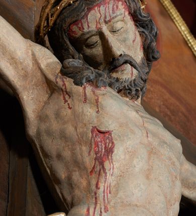 Zdjęcie nr 4: Krucyfiks w typie Christo morte; postać  Chrystusa umarłego przybitego do krzyża trzema gwoździami. Sylwetka w delikatnym zwisie, o silnie zaznaczonej anatomii ciała, z podkreśloną linią żeber i zaznaczonymi śladami męki. Perizonium w formie tkaniny przewiązanej na sznurze, sięgające kolan i odsłaniające prawe udo; z prawej strony spływające kaskadowo. Twarz Jezusa podłużna opadająca na prawe ramię, okolona zarostem; oczy zamknięte, nos podłużny, wystające kości policzkowe; włosy długie spływające na prawe ramię, na głowie złota korona cierniowa. Partie ciała polichromowane naturalistycznie, korona cierniowa i perizonium złocone.