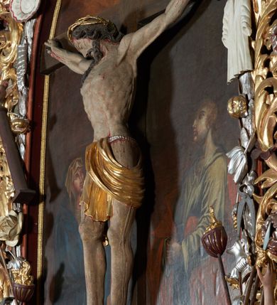 Zdjęcie nr 3: Krucyfiks w typie Christo morte; postać  Chrystusa umarłego przybitego do krzyża trzema gwoździami. Sylwetka w delikatnym zwisie, o silnie zaznaczonej anatomii ciała, z podkreśloną linią żeber i zaznaczonymi śladami męki. Perizonium w formie tkaniny przewiązanej na sznurze, sięgające kolan i odsłaniające prawe udo; z prawej strony spływające kaskadowo. Twarz Jezusa podłużna opadająca na prawe ramię, okolona zarostem; oczy zamknięte, nos podłużny, wystające kości policzkowe; włosy długie spływające na prawe ramię, na głowie złota korona cierniowa. Partie ciała polichromowane naturalistycznie, korona cierniowa i perizonium złocone.
