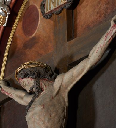Zdjęcie nr 6: Krucyfiks w typie Christo morte; postać  Chrystusa umarłego przybitego do krzyża trzema gwoździami. Sylwetka w delikatnym zwisie, o silnie zaznaczonej anatomii ciała, z podkreśloną linią żeber i zaznaczonymi śladami męki. Perizonium w formie tkaniny przewiązanej na sznurze, sięgające kolan i odsłaniające prawe udo; z prawej strony spływające kaskadowo. Twarz Jezusa podłużna opadająca na prawe ramię, okolona zarostem; oczy zamknięte, nos podłużny, wystające kości policzkowe; włosy długie spływające na prawe ramię, na głowie złota korona cierniowa. Partie ciała polichromowane naturalistycznie, korona cierniowa i perizonium złocone.