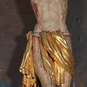Zdjęcie nr 1: Krucyfiks w typie Christo morte; postać  Chrystusa umarłego przybitego do krzyża trzema gwoździami. Sylwetka w delikatnym zwisie, o silnie zaznaczonej anatomii ciała, z podkreśloną linią żeber i zaznaczonymi śladami męki. Perizonium w formie tkaniny przewiązanej na sznurze, sięgające kolan i odsłaniające prawe udo; z prawej strony spływające kaskadowo. Twarz Jezusa podłużna opadająca na prawe ramię, okolona zarostem; oczy zamknięte, nos podłużny, wystające kości policzkowe; włosy długie spływające na prawe ramię, na głowie złota korona cierniowa. Partie ciała polichromowane naturalistycznie, korona cierniowa i perizonium złocone.