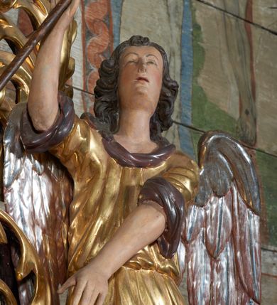 Zdjęcie nr 4: 1. Rzeźba po prawej stronie ołtarza
Figura pełnoplastyczna, stojąca w kontrapoście, prawa ręka uniesiona trzymająca włócznię, lewa skierowana ku dołowi, głowa skierowana ku górze. Twarz podłużna, pełna o drobnych oczach, nosie i ustach. Włosy ciemne, kręcone sięgające do szyi. Anioł ubrany w długą suknię, odkrywająca prawą nogę. Polichromia naturalistyczna w partiach ciała, szata złocona, skrzydła srebrzone. 

2. Rzeźba po lewej stronie ołtarza
Figura pełnoplastyczna, stojąca w kontrapoście, lewa ręka uniesiona w górę wskazuje na arma Christi, zaś prawa jest opuszczona ku dołowi. Głowa aniołą skierowana ku górze. Twarz podłużna, pełna, o drobnych oczach, nosie i ustach. Włosy ciemne, kręcone sięgające szyi. Tunika z podwiniętymi rękawami przepasana sznurem, odkrywająca lewą nogę. Polichromia naturalistyczna w partiach ciała, szata złocona, skrzydła srebrzone.
