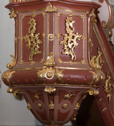 Zdjęcie nr 3: Ambona przyścienna, wisząca ustawiona przy północnej ścianie, dostępna jednobiegowymi schodami z balustradą od strony prezbiterium. Kosz na planie sześcioboku u dołu z ćwierćwałkiem, zdobionym na narożach dekoracją rokokową; u góry zamknięty profilowanym gzymsem. Ścianki artykułowane spływami wolutowymi o karbowanych trzonach. W polach prostokątne płyciny mieszczące płaskorzeźbione rocaille. Podwieszenie w formie stożka o wklęsło-wypukłych bokach, zakończonego płaskorzeźbioną rozetą. Ścianki flankowane w narożach analogicznie jak kosz, w polach trapezoidalne płyciny, przerwane pośrodku okręgiem z rozetką. Zaplecek prostokąty ujęty płaskim obramieniem o zgeometryzowanych wolutach w dolnych narożach oraz rocaille&#039;m w górnych. Pośrodku płaskorzeźbione przedstawienie św. Jana Chrzciciela na tle pejzażu. Baldachim powtarzający plan kosza, zwieńczony wazonem ustawionym na sześciu spiętych kabłąkach. W podniebiu gołębica Ducha Świętego na tle promienistej glorii, na brzegach zawieszony lambrekin. Balustrada schodów pełna, od dołu ujęta półwałkiem, zamknięta profilowanym gzymsem, w polu dwie  płyciny w kształcie rombów, w których umieszczone są rocaille. Balustrada zakończona filarkiem, na którym ustawiony jest wazonik. Całość struktury ambony polichromowana w odcieniach brązu, płaskorzeźba wielobarwna, profilowania i detal architektoniczny pozłacany, podniebienie baldachimu malowane na niebiesko, lambrekin posrebrzany.

