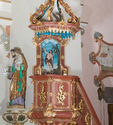 Zdjęcie nr 1: Ambona przyścienna, wisząca ustawiona przy północnej ścianie, dostępna jednobiegowymi schodami z balustradą od strony prezbiterium. Kosz na planie sześcioboku u dołu z ćwierćwałkiem, zdobionym na narożach dekoracją rokokową; u góry zamknięty profilowanym gzymsem. Ścianki artykułowane spływami wolutowymi o karbowanych trzonach. W polach prostokątne płyciny mieszczące płaskorzeźbione rocaille. Podwieszenie w formie stożka o wklęsło-wypukłych bokach, zakończonego płaskorzeźbioną rozetą. Ścianki flankowane w narożach analogicznie jak kosz, w polach trapezoidalne płyciny, przerwane pośrodku okręgiem z rozetką. Zaplecek prostokąty ujęty płaskim obramieniem o zgeometryzowanych wolutach w dolnych narożach oraz rocaille'm w górnych. Pośrodku płaskorzeźbione przedstawienie św. Jana Chrzciciela na tle pejzażu. Baldachim powtarzający plan kosza, zwieńczony wazonem ustawionym na sześciu spiętych kabłąkach. W podniebiu gołębica Ducha Świętego na tle promienistej glorii, na brzegach zawieszony lambrekin. Balustrada schodów pełna, od dołu ujęta półwałkiem, zamknięta profilowanym gzymsem, w polu dwie  płyciny w kształcie rombów, w których umieszczone są rocaille. Balustrada zakończona filarkiem, na którym ustawiony jest wazonik. Całość struktury ambony polichromowana w odcieniach brązu, płaskorzeźba wielobarwna, profilowania i detal architektoniczny pozłacany, podniebienie baldachimu malowane na niebiesko, lambrekin posrebrzany.

