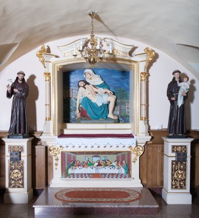 Zdjęcie nr 1: Niewielki ołtarz boczny posadowiony na jednostopniowej, granitowej podstawie. Ołtarz prostopadłościenny, mensa drewniana, w polu antependium płaskorzeźbiona scena przedstawiająca Ostatnią Wieczerzę w prostokątnej ramie, od spodu ujęta profilowanym cokolikiem. W górnych narożach antepedium neorokokowe ornamenty. Nastawa w formie zbliżonej do kwadratu, stojąca bezpośrednio na ołtarzu, flankowana ustawionymi pod kątem kolumienkami na cokołach, które wspierają niepełne, przerwane belkowanie. Kolumny na bazach, trzony marmoryzowane, w jednej trzeciej wysokości przedzielone opaską, kapitele stylizowane na korynckie. Pole główne w kształcie zbliżonym do kwadratu, zamknięte łukiem odcinkowym, u dołu dwa stopnie, wyżej płaskorzeźba przedstawiająca Pietę na tle malowanej Golgoty. Zwieńczenie w formie przerywanego, falującego przyczółka, u dołu zdobionego kratką. Imposty nad kolumnami dekorowane neorokokowym ornamentem. Struktura polichromowana w kolorze jasnego beżu, trzony kolumn marmoryzowane na kolor jasnoróżowy z czerwonym żyłkowaniem, ornamentyka i profilowania złocone. Po bokach ołtarza na wolnostojących cokołach ustawione są rzeźby: św. Franciszka po lewej stronie i św. Antoniego po prawej.