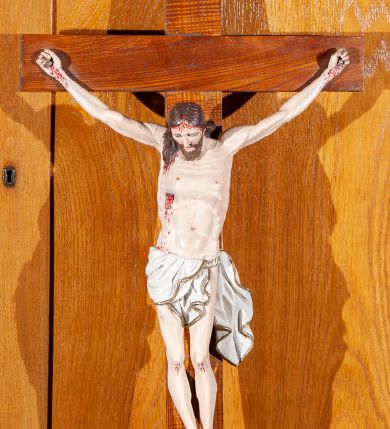 Zdjęcie nr 1: Rzeźba Chrystusa pełnoplastyczna przybita do krzyża trzema gwoździami. Sylwetka delikatnie wygięta, ciało zawieszone w dużym zwisie z wyraźnie zaznaczoną anatomią, stopy przebite jednym gwoździem w układzie prawa na lewą, głowa pochylona do przodu. Twarz szczupła, z delikatnie rozchylonymi ustami, długim i prostym nosem, otwartymi oczami, okolona średniej długości brodą zwiniętą na końcu w dwa pukle. Włosy długie, brązowe, z przedziałkiem pośrodku opadające na plecy i do przodu z prawej strony, rzeźbione w równoległe fale. Na ciele widoczne ślady męki. Białe perizonium zawieszone na sznurze, zdobione na brzegach złotą lamówką z jednym końcem rozwianym wzdłuż lewego uda, odsłaniające nagie, lewe biodro. Krzyż prosty, w kolorze naturalnego drewna. U szczytu pionowej belki titulus w formie banderoli z napisem „IN / RI”. Polichromia w odsłoniętych partiach ciała naturalistyczna. 