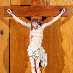 Zdjęcie nr 1: Rzeźba Chrystusa pełnoplastyczna przybita do krzyża trzema gwoździami. Sylwetka delikatnie wygięta, ciało zawieszone w dużym zwisie z wyraźnie zaznaczoną anatomią, stopy przebite jednym gwoździem w układzie prawa na lewą, głowa pochylona do przodu. Twarz szczupła, z delikatnie rozchylonymi ustami, długim i prostym nosem, otwartymi oczami, okolona średniej długości brodą zwiniętą na końcu w dwa pukle. Włosy długie, brązowe, z przedziałkiem pośrodku opadające na plecy i do przodu z prawej strony, rzeźbione w równoległe fale. Na ciele widoczne ślady męki. Białe perizonium zawieszone na sznurze, zdobione na brzegach złotą lamówką z jednym końcem rozwianym wzdłuż lewego uda, odsłaniające nagie, lewe biodro. Krzyż prosty, w kolorze naturalnego drewna. U szczytu pionowej belki titulus w formie banderoli z napisem „IN / RI”. Polichromia w odsłoniętych partiach ciała naturalistyczna. 
