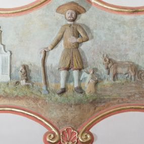 Zdjęcie nr 1: Płaskorzeźba ujęta w fantazyjną ramę utworzoną z zawijających się do środka wolut w kształcie litery „C” spiętych palmetami. Pośrodku ukazany św. Izydor Oracz stojący frontalnie w lekkim rozkroku z prawą ręką wspartą o laskę, lewą złożoną na piersi. Twarz szeroka, okolona krótką brodą. Święty ubrany jest w krótkie, czerwone spodnie, sukmanę sięgająca kolan oraz kapelusz, na stopach ma pełne, brązowe buty. Po prawej stronie kompozycji, u stóp  świętego  klęczący anioł. W tle pejzaż z bryłą kościoła w Podwilku i klęczącą przed nim postacią ukazaną po lewej stronie, natomiast po prawej pług zaprzężony do dwóch wołów, prowadzony przez anioła. Polichromia w odcieniach pastelowych, tunika i kapelusz świętego brązowy, kościół biały nakryty czerwonym dachem. Obramienie polichromii malowane na czerwono, pośrodku złocone, palmety malowane na niebiesko i złocone. Poniżej płaskorzeźby pole w kształcie leżącego prostokąta o wklęsłych narożach z napisem „Labore praeCIpVe pIIs eXpenIs sVbDlicae pLebIs hVIVs / paroChIae s VbViLkensIs haeC saCra aeDes feLICIter / sVrreXIt”.
