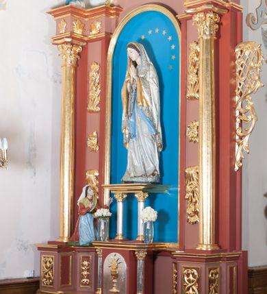 Zdjęcie nr 2: Nastawa ołtarzowa przyścienna, architektoniczna, jednoosiowa, jednokondygnacyjna ze zwieńczeniem. Ołtarz skrzyniowy, prostopadłościenny z kamiennym portatylem w drewnianej ramie. Antepedium drewniane, zdobione płyciną, w której umieszczony jest monogram Matki Boskiej. Po bokach płaskorzeźbione gałązki kwiatów. Tabernakulum w formie prostopadłościennej szafki flankowanej parą wolnostojących kolumienek o korynckich kapitelach, podtrzymujących profilowany gzyms płyty nakrywającej całość obiektu. Drzwiczki w formie zbliżonej do kwadratu, zamknięte półkoliście, zdobione płaskorzeźbioną dekoracją ukazującą kielich z hostią. 

Retabulum ustawione na wysokim, zdwojonym, uskokowym cokole. Nastawa ujęta parą kolumn korynckich. Kolumny wspierają przerwane, wyłamane ponad nimi belkowanie z wysuniętym gzymsem. Pola środkowe w formie prostokątnej wnęki zamkniętej półkoliście, ujętej profilowaną ramą. Wewnątrz pola rzeźba Matki Boskiej ustawiona na wsporniku, wspartym na dwóch kolumienkach. Po lewej stronie rzeźba św. Bernadetty z Soubirous. Tło malowane na kolor błękitny. W partii fryzu motyw stylizowanej palmety. Po bokach nastawy uszy z liści akantu oplatające kratkę regencyjną. W pionowych polach flankujących główną scenę ołtarza ornamentyka roślinna liści akantu z rozetami, pomiędzy nimi motyw kwiatu róży. 

Zwieńczenie o formie wklęsło-wypukłej, ujęte dekoracyjnymi spływami o formach roślinnych. W polu płaskorzeźba przedstawiająca popiersie św. Maksymiliana Marii Kolbego. Po bokach zwieńczenia dwie rzeźby aniołów. Polichromia całości struktury ołtarza w odcieniach brązu, profilowania, detal architektoniczny i ornamentyka złocone i srebrzone.  





