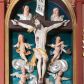 Zdjęcie nr 1: Pełnoplastyczna, polichromowana figura Chrystusa w typie Cristo morte przybitego trzema gwoździami do  dużego, brązowego krzyża. Chrystus ukazany w statycznej pozie, w mocnym zwisie z ugiętymi w kolanach nogami. Twarz podłużna z długim nosem, okolona krótką brodą, która na końcu zawija się w dwa pukle. Włosy długie, ciemnobrązowe opadające na prawe ramię i plecy. Sylwetka szczupła o wyraźnie podkreślonej linii żeber z guzowatą klatką piersiową; na głowie, kolanach, dłoniach, stopach i boku ślady krwi.  Perizonium przewiązane na prawym boku ze zwisem wzdłuż prawego uda, złocone. Na głowie szeroka korona cierniowa, wokół niej niekompletny nimb krzyżowy z jedną wiązką promieni. Kolorystyka ciała utrzymana w odcieniach bladego  beżu. U góry pionowej belki posrebrzany titulus w formie pionowej pogiętej banderoli z napisem: „IN / RI”. Krucyfiks otaczają cztery aniołki na obłokach o teatralnych gestach, nad krzyżem dwie uskrzydlone główki anielskie. Tło malowane na kolor ciemnoniebieski. Polichromia w odsłoniętych partiach ciała naturalistyczna, detale złocone i srebrzone.