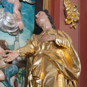 Zdjęcie nr 1: Rzeźba drążona, polichromowana, umiejscowiona na niewielkim, prostopadłościennym cokole. Święty Jan w ujęciu całopostaciowym, w pozycji stojącej, w kontrapoście z głową uniesioną ku górze i lekko odchyloną do tyłu i w prawo. Twarz owalna o mocno zarysowanym podbródku, nos długi, lekko zadarty, szpiczasty, usta niewielkie, lekko rozchylone, oczy zwrócone ku górze. Włosy długie, brązowe, falowane, opadające na plecy. Lewa dłoń wsparta na piersiach, prawa wyciągnięta ku przodowi. Święty ubrany jest w długą, fałdowaną, przewiązaną w pasie suknię z kołnierzykiem pod szyją, spod niej widoczne bose stopy. Na niej płaszcz przerzucony, przez prawe ramię i przełożony przez pasek podtrzymujący suknię. Polichromia w odsłoniętych partiach ciała naturalistyczna, szaty złocone.