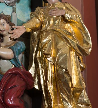 Zdjęcie nr 2: Rzeźba drążona, polichromowana, umiejscowiona na niewielkim, prostopadłościennym cokole. Święty Jan w ujęciu całopostaciowym, w pozycji stojącej, w kontrapoście z głową uniesioną ku górze i lekko odchyloną do tyłu i w prawo. Twarz owalna o mocno zarysowanym podbródku, nos długi, lekko zadarty, szpiczasty, usta niewielkie, lekko rozchylone, oczy zwrócone ku górze. Włosy długie, brązowe, falowane, opadające na plecy. Lewa dłoń wsparta na piersiach, prawa wyciągnięta ku przodowi. Święty ubrany jest w długą, fałdowaną, przewiązaną w pasie suknię z kołnierzykiem pod szyją, spod niej widoczne bose stopy. Na niej płaszcz przerzucony, przez prawe ramię i przełożony przez pasek podtrzymujący suknię. Polichromia w odsłoniętych partiach ciała naturalistyczna, szaty złocone.