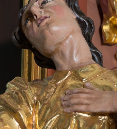 Zdjęcie nr 3: Rzeźba drążona, polichromowana, umiejscowiona na niewielkim, prostopadłościennym cokole. Święty Jan w ujęciu całopostaciowym, w pozycji stojącej, w kontrapoście z głową uniesioną ku górze i lekko odchyloną do tyłu i w prawo. Twarz owalna o mocno zarysowanym podbródku, nos długi, lekko zadarty, szpiczasty, usta niewielkie, lekko rozchylone, oczy zwrócone ku górze. Włosy długie, brązowe, falowane, opadające na plecy. Lewa dłoń wsparta na piersiach, prawa wyciągnięta ku przodowi. Święty ubrany jest w długą, fałdowaną, przewiązaną w pasie suknię z kołnierzykiem pod szyją, spod niej widoczne bose stopy. Na niej płaszcz przerzucony, przez prawe ramię i przełożony przez pasek podtrzymujący suknię. Polichromia w odsłoniętych partiach ciała naturalistyczna, szaty złocone.
