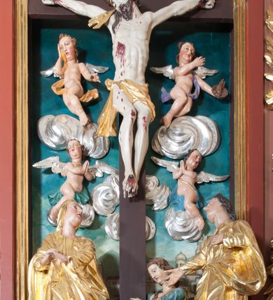 Zdjęcie nr 1: Rzeźba wolnostojąca, wydrążona, umieszczona  na srebrzonej podstawie imitującej kamień. Święta Maria Magdalena przedstawiona w ujęciu całopostaciowym, w pozycji klęczącej, zwrócona w trzech czwartych w prawo, oburącz obejmująca krzyż. Twarz pełna, oczy opuszczone w dół, przymknięte, nos i usta niewielkie. Karnacja jasna o zaróżowionych policzkach. Włosy długie, falowane, brązowe, opadające na plecy i prawe ramię. Ubrana jest w długą biało-błękitną suknię z szerokimi, podwiniętymi rękawami oraz czerwony płaszcz okrywający część pleców i lewą nogę. Polichromia w odsłoniętych partiach ciała naturalistyczna.