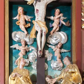 Zdjęcie nr 1: Rzeźba wolnostojąca, wydrążona, umieszczona  na srebrzonej podstawie imitującej kamień. Święta Maria Magdalena przedstawiona w ujęciu całopostaciowym, w pozycji klęczącej, zwrócona w trzech czwartych w prawo, oburącz obejmująca krzyż. Twarz pełna, oczy opuszczone w dół, przymknięte, nos i usta niewielkie. Karnacja jasna o zaróżowionych policzkach. Włosy długie, falowane, brązowe, opadające na plecy i prawe ramię. Ubrana jest w długą biało-błękitną suknię z szerokimi, podwiniętymi rękawami oraz czerwony płaszcz okrywający część pleców i lewą nogę. Polichromia w odsłoniętych partiach ciała naturalistyczna.