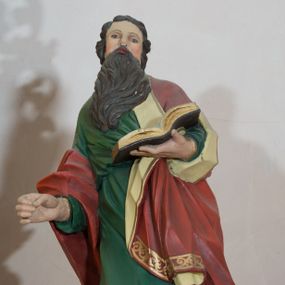 Zdjęcie nr 1: Rzeźba drążona, przedstawiająca św. Pawła. Święty ustawiony na niskim, brązowym cokole, frontalnie, w kontrapoście, o esowato wygiętej sylwetce, z prawą nogą ugiętą w kolanie, głową zwróconą w lewo. W lewej dłoni trzyma otwartą księgę, natomiast prawą ma wysuniętą do przodu i ułożoną do niezachowanego atrybutu (miecza). Twarz owalna z zarumienionymi policzkami z dużym nosem, okolona ciemnobrązową, gęstą i długą brodą. Włosy średniej długości, ciemnobrązowe, zasłaniają uszy. Ubrany jest w długą w zieloną suknię oraz czerwony płaszcz z beżową podszewką, założony na lewe ramię i przerzucony jedną połą przez prawe przedramię. Płaszcz na brzegach zdobiony jest złoconą dekoracją ornamentalną, a suknia u dołu dekorowana ornamentem złożonym ze złączonych trójliści. Polichromia w odsłoniętych partiach ciała naturalistyczna, detale złocone. 