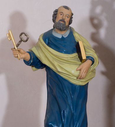 Zdjęcie nr 1: Rzeźba drążona, przedstawiająca św. Piotra. Święty ustawiony na niskim cokole, w delikatnym kontrapoście, z prawą nogą ugiętą w kolanie, z rozłożonymi na boki stopami. W prawej dłoni trzyma dwa skrzyżowane klucze, a w lewej księgę w brązowej oprawie. Twarz podłużna, okolona siwą brodą z długim nosem i małymi ustami. Włosy siwe, zasłaniające uszy, głowa ujęta do połowy łysiną, nad czołem kosmyk siwych włosów. Święty jest ubrany w długą, niebieską suknię z kołnierzykiem, u dołu zdobioną złoconym pasem ornamentu składającego się ze złączonych trójliści. Na suknię ma założony zwinięty jasnozielony płaszcz. Polichromia w odsłoniętych partiach ciała naturalistyczna, detale i klucze złocone.
