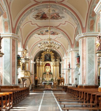 Zdjęcie nr 3: Kościół usytuowany jest w centrum miejscowości na północ od głównej drogi. Na plac kościelny prowadzi główne wejście od strony wschodniej. Świątynia skierowana jest na północ, założona na planie prostokąta z wieżą w fasadzie z prezbiterium zamkniętym trójbocznie, węższym od nawy. Za prezbiterium dobudowana jest kaplica na planie prostokąta, a od zachodu zakrystia. Główne wejście do kościoła znajduje się od strony południowej. 

Wnętrze trójnawowe, halowe, czteroprzęsłowe; nawy oddzielone arkadami na opliastrowanych filarach o wklęsłych narożnikach wspierających sklepienie żaglaste na gurtach. Chór muzyczny wsparty na trzech arkadach filarowych. Balustrada na rzucie wklęsło-wypukłym z uskokami. Wnętrze nawy jest oświetlone przez dziesięć, niskich, zamkniętych półkoliście okien, w prezbiterium cztery analogiczne okna. 

Fasada z ryzalitem w osi środkowej, ujętym zdwojonymi pilastrami, zwieńczonym przerwanym przyczółkiem, na osi portal i balkon z półkoliście zamkniętym oknem. W szczycie fasady drugi przyczółek, w polu monogram maryjny, a poniżej napis: „AVE MARIA GRATIA PLENA DOMINVS TECTVM”. Wyżej na osi czworoboczna wieża, opięta pilastrami w narożach, zwieńczona baniastym hełmem z latarnią. Korpus nawowy o zaokrąglonych narożnikach z podziałami ramowymi i oknami termalnymi. Prezbiterium i kaplica opięte szkarpami. Nad prezbiterium i nawą oddzielne dachy, dwuspadowe. 
