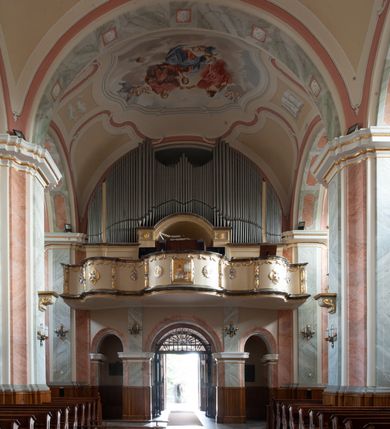 Zdjęcie nr 7: Kościół usytuowany jest w centrum miejscowości na północ od głównej drogi. Na plac kościelny prowadzi główne wejście od strony wschodniej. Świątynia skierowana jest na północ, założona na planie prostokąta z wieżą w fasadzie z prezbiterium zamkniętym trójbocznie, węższym od nawy. Za prezbiterium dobudowana jest kaplica na planie prostokąta, a od zachodu zakrystia. Główne wejście do kościoła znajduje się od strony południowej. 

Wnętrze trójnawowe, halowe, czteroprzęsłowe; nawy oddzielone arkadami na opliastrowanych filarach o wklęsłych narożnikach wspierających sklepienie żaglaste na gurtach. Chór muzyczny wsparty na trzech arkadach filarowych. Balustrada na rzucie wklęsło-wypukłym z uskokami. Wnętrze nawy jest oświetlone przez dziesięć, niskich, zamkniętych półkoliście okien, w prezbiterium cztery analogiczne okna. 

Fasada z ryzalitem w osi środkowej, ujętym zdwojonymi pilastrami, zwieńczonym przerwanym przyczółkiem, na osi portal i balkon z półkoliście zamkniętym oknem. W szczycie fasady drugi przyczółek, w polu monogram maryjny, a poniżej napis: „AVE MARIA GRATIA PLENA DOMINVS TECTVM”. Wyżej na osi czworoboczna wieża, opięta pilastrami w narożach, zwieńczona baniastym hełmem z latarnią. Korpus nawowy o zaokrąglonych narożnikach z podziałami ramowymi i oknami termalnymi. Prezbiterium i kaplica opięte szkarpami. Nad prezbiterium i nawą oddzielne dachy, dwuspadowe. 
