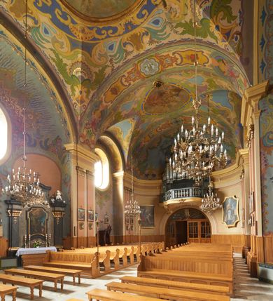 Zdjęcie nr 17: Polichromia pokrywa zarówno powierzchnię ścian, jak i sklepień kościoła, jednak zdecydowanie bardziej dekoracyjne motywy pojawiają się w górnych partiach murów. Dominuje stylizowana ornamentyka roślinna na błękitnym tle, utrzymana w jasnych, żywych tonacjach zróżnicowanych kolorów. Szerokie bordiury o tworzących je fantazyjnych formach i roślinności ujmują niewielkich rozmiarów sceny figuralne umiejscowione pośrodku sklepienia każdego z przęseł kościoła. Kompozycje, o zbliżonych do owalu kształtach przedstawiają: Śmierć św. Józefa w ostatnim przęśle nawy, Ukoronowanie Matki Boskiej na przecięciu nawy z transeptem oraz Wniebowzięcie Najświętszej Marii Panny w przęśle prezbiterium. W konsze absydy ukazana jest scena adoracji kielicha eucharystycznego przez anioły o tęczowych skrzydłach, ubrane w barwne, wzorzyste szaty. Po lewej stronie kościoła, na ścianie transeptu jest ukazana na tle pejzażu scena Chrztu Jezusa. 