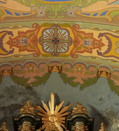 Zdjęcie nr 19: Polichromia pokrywa zarówno powierzchnię ścian, jak i sklepień kościoła, jednak zdecydowanie bardziej dekoracyjne motywy pojawiają się w górnych partiach murów. Dominuje stylizowana ornamentyka roślinna na błękitnym tle, utrzymana w jasnych, żywych tonacjach zróżnicowanych kolorów. Szerokie bordiury o tworzących je fantazyjnych formach i roślinności ujmują niewielkich rozmiarów sceny figuralne umiejscowione pośrodku sklepienia każdego z przęseł kościoła. Kompozycje, o zbliżonych do owalu kształtach przedstawiają: Śmierć św. Józefa w ostatnim przęśle nawy, Ukoronowanie Matki Boskiej na przecięciu nawy z transeptem oraz Wniebowzięcie Najświętszej Marii Panny w przęśle prezbiterium. W konsze absydy ukazana jest scena adoracji kielicha eucharystycznego przez anioły o tęczowych skrzydłach, ubrane w barwne, wzorzyste szaty. Po lewej stronie kościoła, na ścianie transeptu jest ukazana na tle pejzażu scena Chrztu Jezusa. 