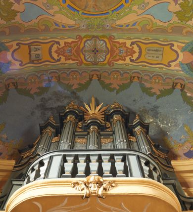 Zdjęcie nr 18: Polichromia pokrywa zarówno powierzchnię ścian, jak i sklepień kościoła, jednak zdecydowanie bardziej dekoracyjne motywy pojawiają się w górnych partiach murów. Dominuje stylizowana ornamentyka roślinna na błękitnym tle, utrzymana w jasnych, żywych tonacjach zróżnicowanych kolorów. Szerokie bordiury o tworzących je fantazyjnych formach i roślinności ujmują niewielkich rozmiarów sceny figuralne umiejscowione pośrodku sklepienia każdego z przęseł kościoła. Kompozycje, o zbliżonych do owalu kształtach przedstawiają: Śmierć św. Józefa w ostatnim przęśle nawy, Ukoronowanie Matki Boskiej na przecięciu nawy z transeptem oraz Wniebowzięcie Najświętszej Marii Panny w przęśle prezbiterium. W konsze absydy ukazana jest scena adoracji kielicha eucharystycznego przez anioły o tęczowych skrzydłach, ubrane w barwne, wzorzyste szaty. Po lewej stronie kościoła, na ścianie transeptu jest ukazana na tle pejzażu scena Chrztu Jezusa. 