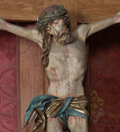 Zdjęcie nr 1: Rzeźba ścięta z tyłu, przybita do krzyża trzema gwoździami, w typie Christo vivo. Ciało w lekkim zwisie o horyzontalnie rozłożonych ramionach, głowa opada na prawy bark, nogi lekko ugięte, stopy skrzyżowane w układzie prawa na lewą. Ciało jest silnie wysmuklone, z wyraźnie rozbudowaną i wypchniętą do przodu klatką piersiową, z podkreślonymi żebrami i zapadłym brzuchem; ręce i nogi są bardzo wychudzone z wyłamanymi barkami, podkreślonymi łokciami i kolanami. Twarz jest pociągła, wychudzona, z głęboko osadzonymi i rzeźbionymi, półotwartymi oczami, wąskim, długim nosem oraz otwartymi ustami z opadającą żuchwą; okolona krótką brodą, głęboko rzeźbioną w regularne pukle oraz długimi włosami ułożonymi w pojedyncze lekko skręcone pukle opadające na plecy oraz na klatkę piersiową. Głowę wieńczy masywna korona cierniowa. Perizonium jest krótkie, silnie opasujące ciało, zawiązane w partii podbrzusza z rozwianym ekspresyjnie fragmentem tkaniny w charakterystycznym odwinięciu na prawym boku. Figura jest polichromowana naturalistycznie, ciało wyróżnia się bladą karnacją z zaznaczonymi śladami męki; perizonium jest złocone i niebieskie na podszewce.
