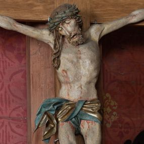 Zdjęcie nr 1: Rzeźba ścięta z tyłu, przybita do krzyża trzema gwoździami, w typie Christo vivo. Ciało w lekkim zwisie o horyzontalnie rozłożonych ramionach, głowa opada na prawy bark, nogi lekko ugięte, stopy skrzyżowane w układzie prawa na lewą. Ciało jest silnie wysmuklone, z wyraźnie rozbudowaną i wypchniętą do przodu klatką piersiową, z podkreślonymi żebrami i zapadłym brzuchem; ręce i nogi są bardzo wychudzone z wyłamanymi barkami, podkreślonymi łokciami i kolanami. Twarz jest pociągła, wychudzona, z głęboko osadzonymi i rzeźbionymi, półotwartymi oczami, wąskim, długim nosem oraz otwartymi ustami z opadającą żuchwą; okolona krótką brodą, głęboko rzeźbioną w regularne pukle oraz długimi włosami ułożonymi w pojedyncze lekko skręcone pukle opadające na plecy oraz na klatkę piersiową. Głowę wieńczy masywna korona cierniowa. Perizonium jest krótkie, silnie opasujące ciało, zawiązane w partii podbrzusza z rozwianym ekspresyjnie fragmentem tkaniny w charakterystycznym odwinięciu na prawym boku. Figura jest polichromowana naturalistycznie, ciało wyróżnia się bladą karnacją z zaznaczonymi śladami męki; perizonium jest złocone i niebieskie na podszewce.