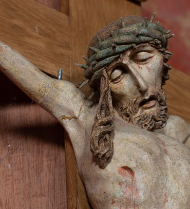 Zdjęcie nr 13: Rzeźba ścięta z tyłu, przybita do krzyża trzema gwoździami, w typie Christo vivo. Ciało w lekkim zwisie o horyzontalnie rozłożonych ramionach, głowa opada na prawy bark, nogi lekko ugięte, stopy skrzyżowane w układzie prawa na lewą. Ciało jest silnie wysmuklone, z wyraźnie rozbudowaną i wypchniętą do przodu klatką piersiową, z podkreślonymi żebrami i zapadłym brzuchem; ręce i nogi są bardzo wychudzone z wyłamanymi barkami, podkreślonymi łokciami i kolanami. Twarz jest pociągła, wychudzona, z głęboko osadzonymi i rzeźbionymi, półotwartymi oczami, wąskim, długim nosem oraz otwartymi ustami z opadającą żuchwą; okolona krótką brodą, głęboko rzeźbioną w regularne pukle oraz długimi włosami ułożonymi w pojedyncze lekko skręcone pukle opadające na plecy oraz na klatkę piersiową. Głowę wieńczy masywna korona cierniowa. Perizonium jest krótkie, silnie opasujące ciało, zawiązane w partii podbrzusza z rozwianym ekspresyjnie fragmentem tkaniny w charakterystycznym odwinięciu na prawym boku. Figura jest polichromowana naturalistycznie, ciało wyróżnia się bladą karnacją z zaznaczonymi śladami męki; perizonium jest złocone i niebieskie na podszewce.