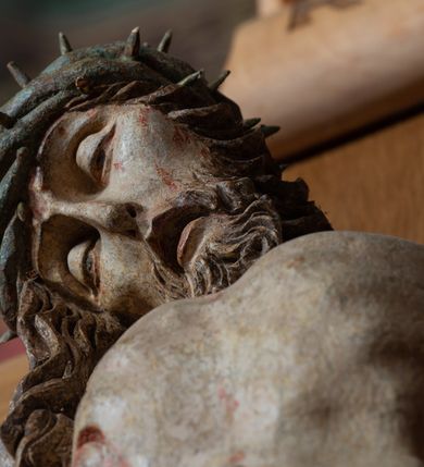 Zdjęcie nr 12: Rzeźba ścięta z tyłu, przybita do krzyża trzema gwoździami, w typie Christo vivo. Ciało w lekkim zwisie o horyzontalnie rozłożonych ramionach, głowa opada na prawy bark, nogi lekko ugięte, stopy skrzyżowane w układzie prawa na lewą. Ciało jest silnie wysmuklone, z wyraźnie rozbudowaną i wypchniętą do przodu klatką piersiową, z podkreślonymi żebrami i zapadłym brzuchem; ręce i nogi są bardzo wychudzone z wyłamanymi barkami, podkreślonymi łokciami i kolanami. Twarz jest pociągła, wychudzona, z głęboko osadzonymi i rzeźbionymi, półotwartymi oczami, wąskim, długim nosem oraz otwartymi ustami z opadającą żuchwą; okolona krótką brodą, głęboko rzeźbioną w regularne pukle oraz długimi włosami ułożonymi w pojedyncze lekko skręcone pukle opadające na plecy oraz na klatkę piersiową. Głowę wieńczy masywna korona cierniowa. Perizonium jest krótkie, silnie opasujące ciało, zawiązane w partii podbrzusza z rozwianym ekspresyjnie fragmentem tkaniny w charakterystycznym odwinięciu na prawym boku. Figura jest polichromowana naturalistycznie, ciało wyróżnia się bladą karnacją z zaznaczonymi śladami męki; perizonium jest złocone i niebieskie na podszewce.