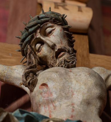Zdjęcie nr 11: Rzeźba ścięta z tyłu, przybita do krzyża trzema gwoździami, w typie Christo vivo. Ciało w lekkim zwisie o horyzontalnie rozłożonych ramionach, głowa opada na prawy bark, nogi lekko ugięte, stopy skrzyżowane w układzie prawa na lewą. Ciało jest silnie wysmuklone, z wyraźnie rozbudowaną i wypchniętą do przodu klatką piersiową, z podkreślonymi żebrami i zapadłym brzuchem; ręce i nogi są bardzo wychudzone z wyłamanymi barkami, podkreślonymi łokciami i kolanami. Twarz jest pociągła, wychudzona, z głęboko osadzonymi i rzeźbionymi, półotwartymi oczami, wąskim, długim nosem oraz otwartymi ustami z opadającą żuchwą; okolona krótką brodą, głęboko rzeźbioną w regularne pukle oraz długimi włosami ułożonymi w pojedyncze lekko skręcone pukle opadające na plecy oraz na klatkę piersiową. Głowę wieńczy masywna korona cierniowa. Perizonium jest krótkie, silnie opasujące ciało, zawiązane w partii podbrzusza z rozwianym ekspresyjnie fragmentem tkaniny w charakterystycznym odwinięciu na prawym boku. Figura jest polichromowana naturalistycznie, ciało wyróżnia się bladą karnacją z zaznaczonymi śladami męki; perizonium jest złocone i niebieskie na podszewce.