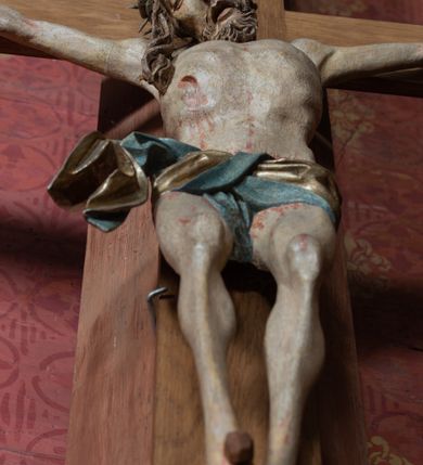 Zdjęcie nr 2: Rzeźba ścięta z tyłu, przybita do krzyża trzema gwoździami, w typie Christo vivo. Ciało w lekkim zwisie o horyzontalnie rozłożonych ramionach, głowa opada na prawy bark, nogi lekko ugięte, stopy skrzyżowane w układzie prawa na lewą. Ciało jest silnie wysmuklone, z wyraźnie rozbudowaną i wypchniętą do przodu klatką piersiową, z podkreślonymi żebrami i zapadłym brzuchem; ręce i nogi są bardzo wychudzone z wyłamanymi barkami, podkreślonymi łokciami i kolanami. Twarz jest pociągła, wychudzona, z głęboko osadzonymi i rzeźbionymi, półotwartymi oczami, wąskim, długim nosem oraz otwartymi ustami z opadającą żuchwą; okolona krótką brodą, głęboko rzeźbioną w regularne pukle oraz długimi włosami ułożonymi w pojedyncze lekko skręcone pukle opadające na plecy oraz na klatkę piersiową. Głowę wieńczy masywna korona cierniowa. Perizonium jest krótkie, silnie opasujące ciało, zawiązane w partii podbrzusza z rozwianym ekspresyjnie fragmentem tkaniny w charakterystycznym odwinięciu na prawym boku. Figura jest polichromowana naturalistycznie, ciało wyróżnia się bladą karnacją z zaznaczonymi śladami męki; perizonium jest złocone i niebieskie na podszewce.
