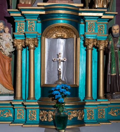 Zdjęcie nr 2: Pełnoplastyczna figura św. Ojca Pio ukazanego w całej postaci, stojącego frontalnie, na niewysokiej podstawie zbliżonej do prostopadłościanu. Głowa jest lekko pochylona w dół. Prawa ręka uniesiona jest w geście błogosławieństwa, lewa wsparta na piersiach. Pociągłą twarz charakteryzują rysy dojrzałego mężczyzny, ciemne, podkrążone oczy oraz półdługi, gęsty, siwy zarost; na głowie są krótkie, siwe włosy. Święty ubrany jest w habit kapucyński przewiązany sznurem, na którym zawieszony jest czarny różaniec. Na ramiona nałożona jest zielona stuła zdobiona reliefowym motywem kłosów zbóż. Dłonie osłaniają szare rękawiczki w typie mitenek. Na stopach są ciemnobrązowe buty z kwadratowymi noskami. Na podstawie znajduje się niewielka tabliczka w formie banderoli z napisem: „O(jciec) PIO”. 