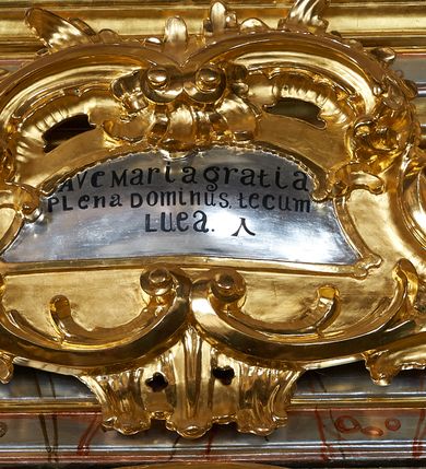 Zdjęcie nr 9: Nastawa ołtarzowa architektoniczna, jednoosiowa, jednokondygnacyjna ze zwieńczeniem. Mensa drewniana o profilowanej krawędzi. Ołtarz  sarkofagowy, na profilowanym cokole; na froncie intarsjowany wzór geometryczny. Kondygnacja ustawiona na cokole, ujęta parą zdwojonych filarów o kapitelach kompozytowych. Podpory dźwigają pełne belkowanie, wyłamane na ich osi, o wklęsło-wypukłym fryzie i silnie wysuniętym gzymsie oraz przerwany wolutowy przyczółek. W polu środkowym profilowana rama w formie stojącego prostokąta zamkniętego łukiem segmentowym nadwieszonym z uskokiem, z obrazem „Zwiastowanie”. Przed filarami, na wklęsło-wypukłych postumentach dwie figury niezidentyfikowanych świętych. Zwieńczenie w formie leżącego prostokąta ujętego spływami wolutowymi, zamkniętego falistym gzymsem przechodzącym w zwrócone przeciwstawnie woluty. W polu rama o fantazyjnej formie zbliżonej do trójkąta z obrazem „Nawiedzenie św. Elżbiety”. Trzony filarów dekorowane kampanulami. W polu środkowym w przyłuczach ornament rocaille&#039;owy. Rama obrazu na dłuższych bokach zdobiona rocaille&#039;m. Nad polem środkowym na belkowaniu rocaille&#039;owy kartusz z napisem w polu „Ave Maria gratia / Plena Dominus tecum / Luea. Ʌ”. W partii fryzu, na osiach podpór z trzech stron rozety. Struktura w całości laserunkowa, srebrzona, marmoryzowana; ornamentyka i profile złocone.