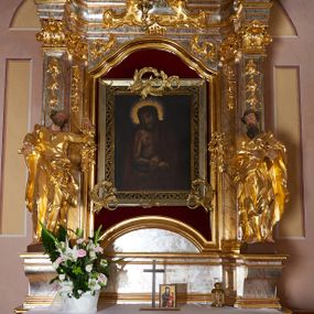Zdjęcie nr 1: Nastawa ołtarzowa architektoniczna, jednoosiowa, jednokondygnacyjna ze zwieńczeniem. Mensa drewniana o profilowanej krawędzi. Ołtarz  sarkofagowy, na profilowanym cokole; na froncie intarsjowany wzór geometryczny. Kondygnacja ustawiona na profilowanym cokole, ujęta parą zdwojonych filarów o kanelowanych trzonach i kapitelach kompozytowych. Podpory dźwigają pełne belkowanie, wyłamane na ich osi, o wklęsło-wypukłym fryzie i silnie wysuniętym gzymsie oraz przerwany wolutowy przyczółek. W polu środkowym profilowana rama w formie stojącego prostokąta zamkniętego łukiem segmentowym nadwieszonym z uskokiem, z mniejszym obrazem wewnątrz w formie stojącego prostokąta, z przedstawieniem Ecce Homo. Przed filarami, na wklęsło-wypukłych postumentach dwie figury niezidentyfikowanych świętych. Zwieńczenie w formie leżącego prostokąta ujętego spływami wolutowymi, zamkniętego falistym gzymsem przechodzącym w zwrócone przeciwstawnie woluty. W polu rama o fantazyjnej formie zbliżonej do trójkąta z obrazem przedstawiającym Narodzenie Marii. Trzony filarów dekorowane kampanulami. W polu środkowym w przyłuczach rocaille. Rama obrazu na dłuższych bokach zdobiona ornamentem rocaille'owym. Nad polem środkowym w polu belkowania racaille'owy kartusz  z napisem: „ECCE HOMO”. W partii fryzu, na osiach podpór z trzech stron rozety. Struktura w całości laserunkowa, srebrzona, marmoryzowana; ornamentyka i profile złocone.