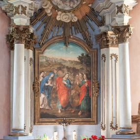 Zdjęcie nr 1: Nastawa ołtarzowa architektoniczna, jednoosiowa, jednokondygnacyjna ze zwieńczeniem w formie promienistej glorii. Ołtarz prostopadłościenny z kamienną mensą. Nastawa wsparta na ukośnie ustawionym cokole, podtrzymującym parę zdwojonych pilastrów i stojącą przed nimi parę kolumn. Podpory wspierają imposty i przerywany, wolutowy przyczółek. Pilastry zdobione wąskimi płycinami, zakończonymi skromnym rocaille’m. Kolumny ustawione na bazach, trzony gładkie, kapitele kompozytowe. Imposty zdobione stylizowanymi rozetami. W polu głównym, w prostokątnej ramie, zamkniętej łukiem nadwieszonym znajduje się obraz „Pożegnanie Chrystusa”. Zwieńczenie w formie monumentalnej promienistej glorii, w polu której umieszczony jest obraz „Wniebowzięcie Najświętszej Marii Panny”, otoczony obłokami. Struktura polichromowana na kolor biały, detale na niebiesko, ornamentyka złocona.
